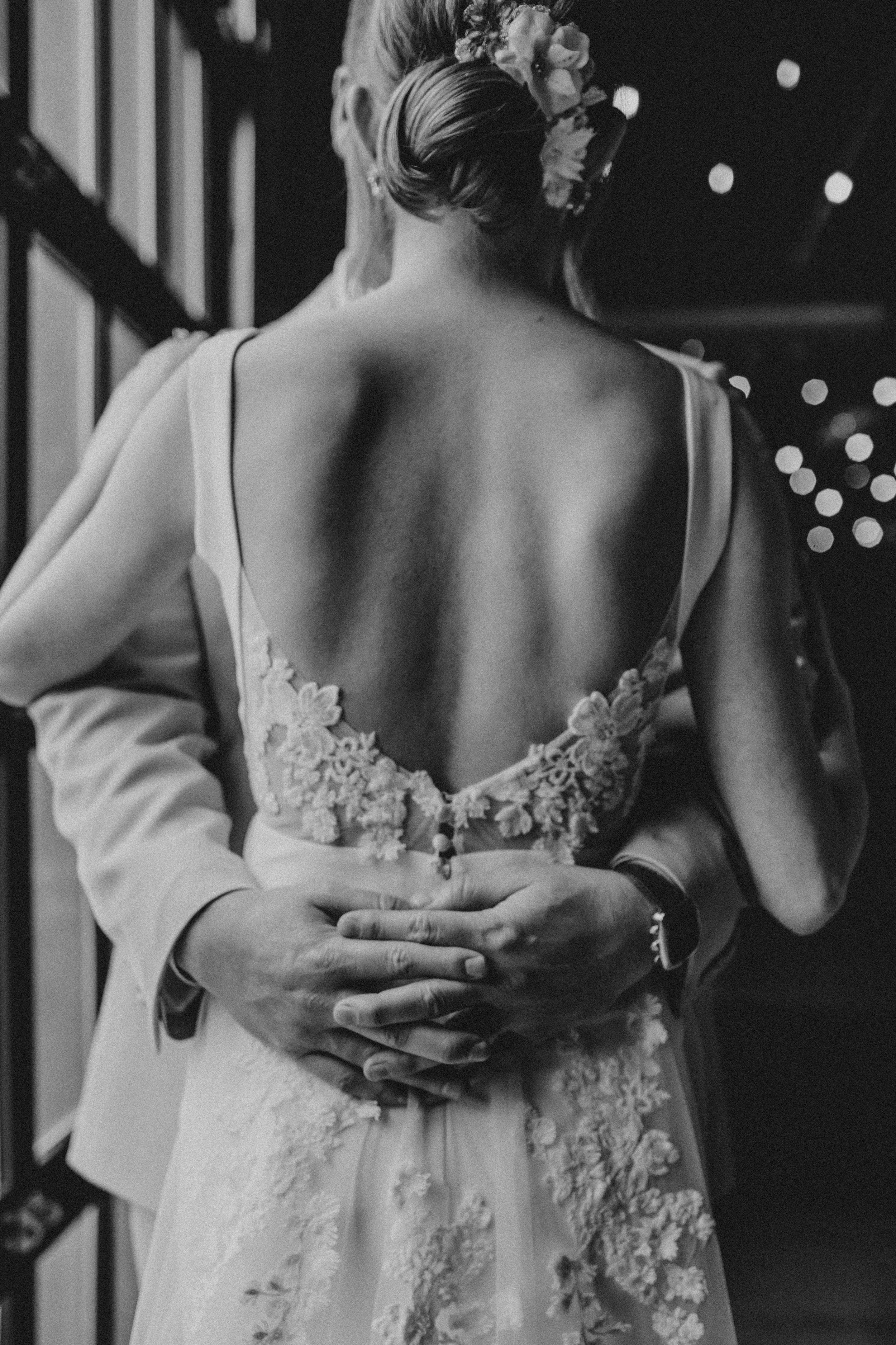 Artistic black and white photo showing back details of a wedding dress with delicate lace and floral accents.
