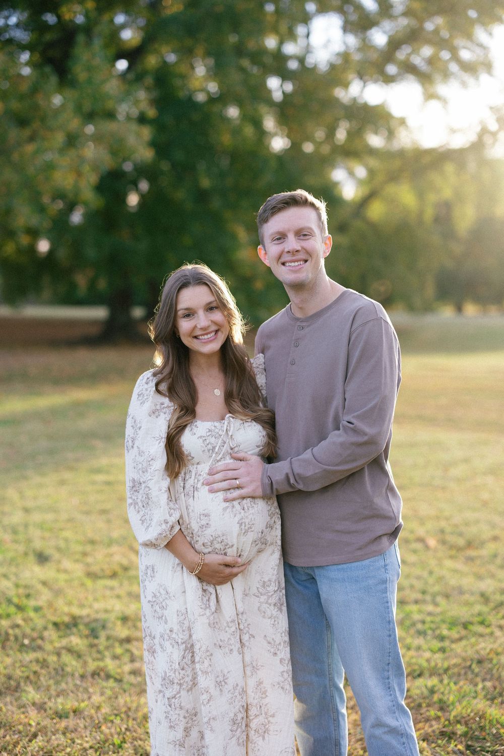 A couple embraces in a sunlit field during golden hour while wearing casual clothing and sharing joyful moments together.