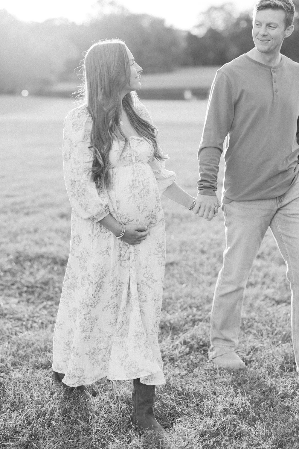 A couple holds hands while walking through a grassy field in black and white.