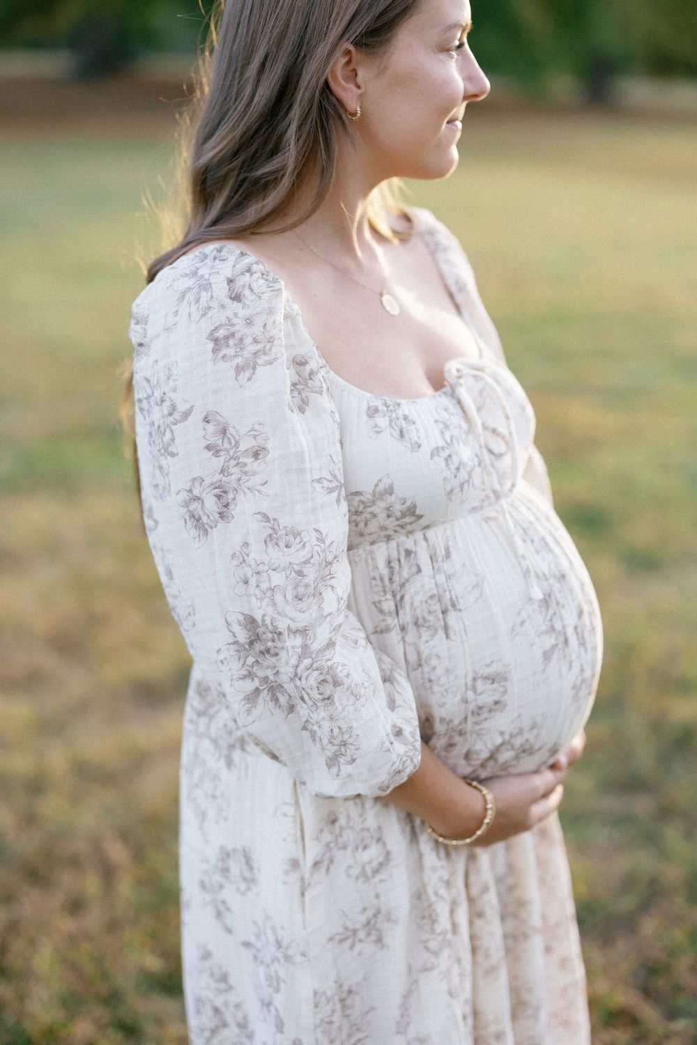 A person in a flowy white floral dress poses outdoors in a field during golden hour.