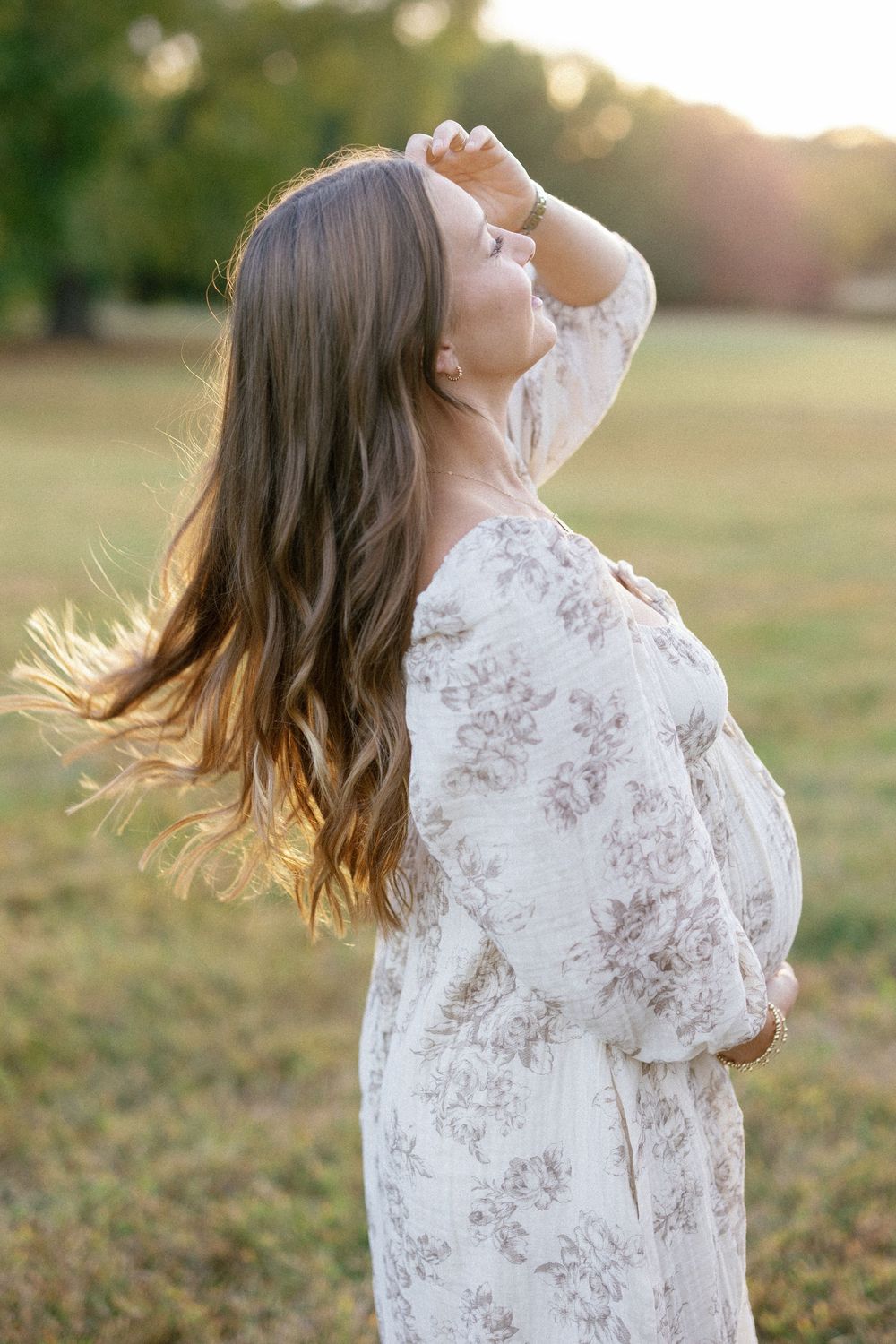 A woman in a white lace dress twirls joyfully in a sunlit field during golden hour.