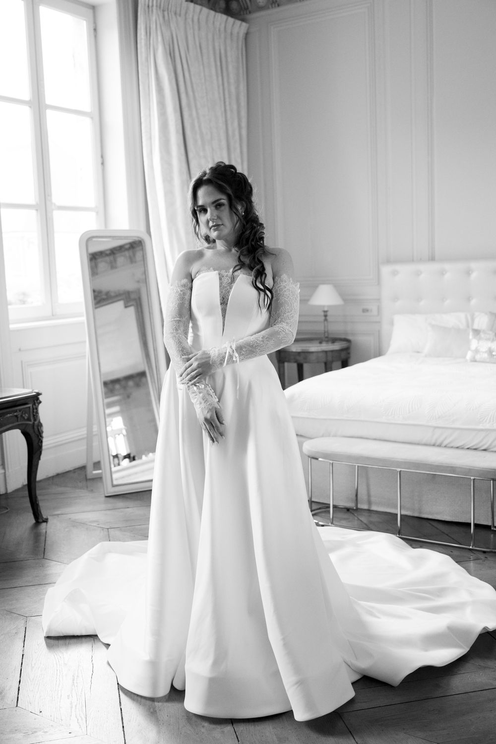 Elegant white wedding gown with long sleeves and plunging neckline photographed in black and white in a bright bedroom.