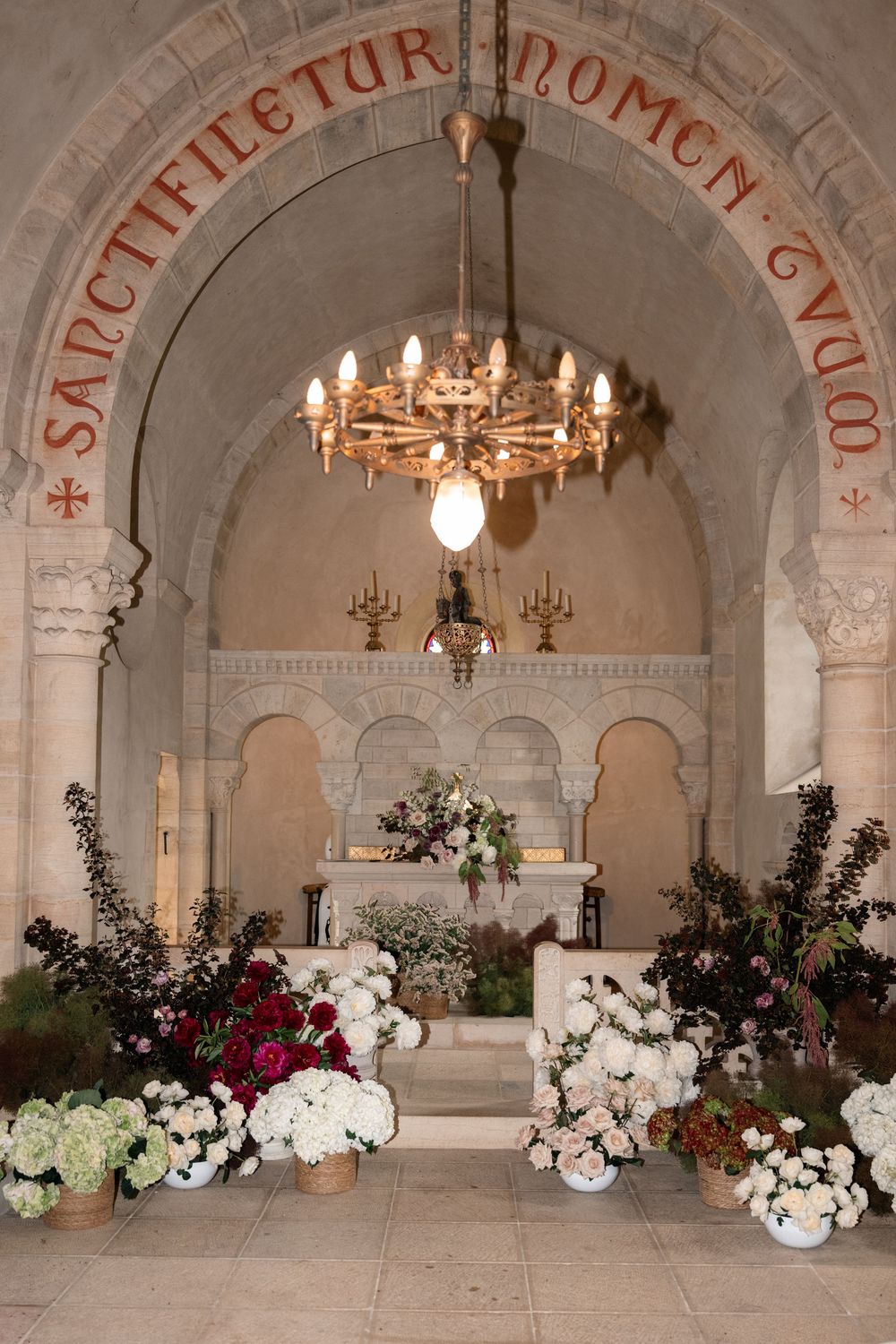 Elegant stone archway decorated with white and red floral arrangements and illuminated by ornate chandeliers.