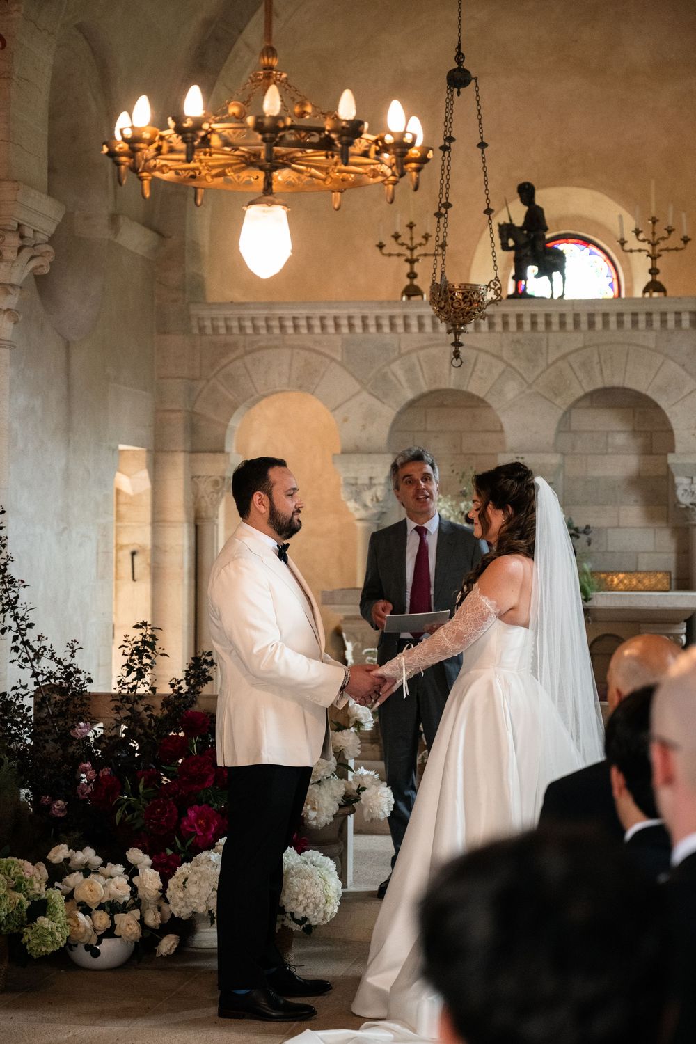 Wedding ceremony in an ornate historic venue with arched architecture and chandelier lighting.