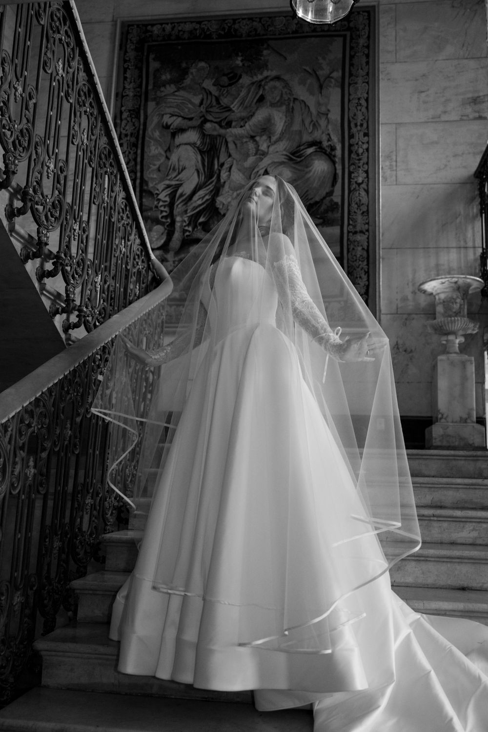 A flowing white wedding dress with layers of tulle and a long veil is photographed in a series of elegant poses.