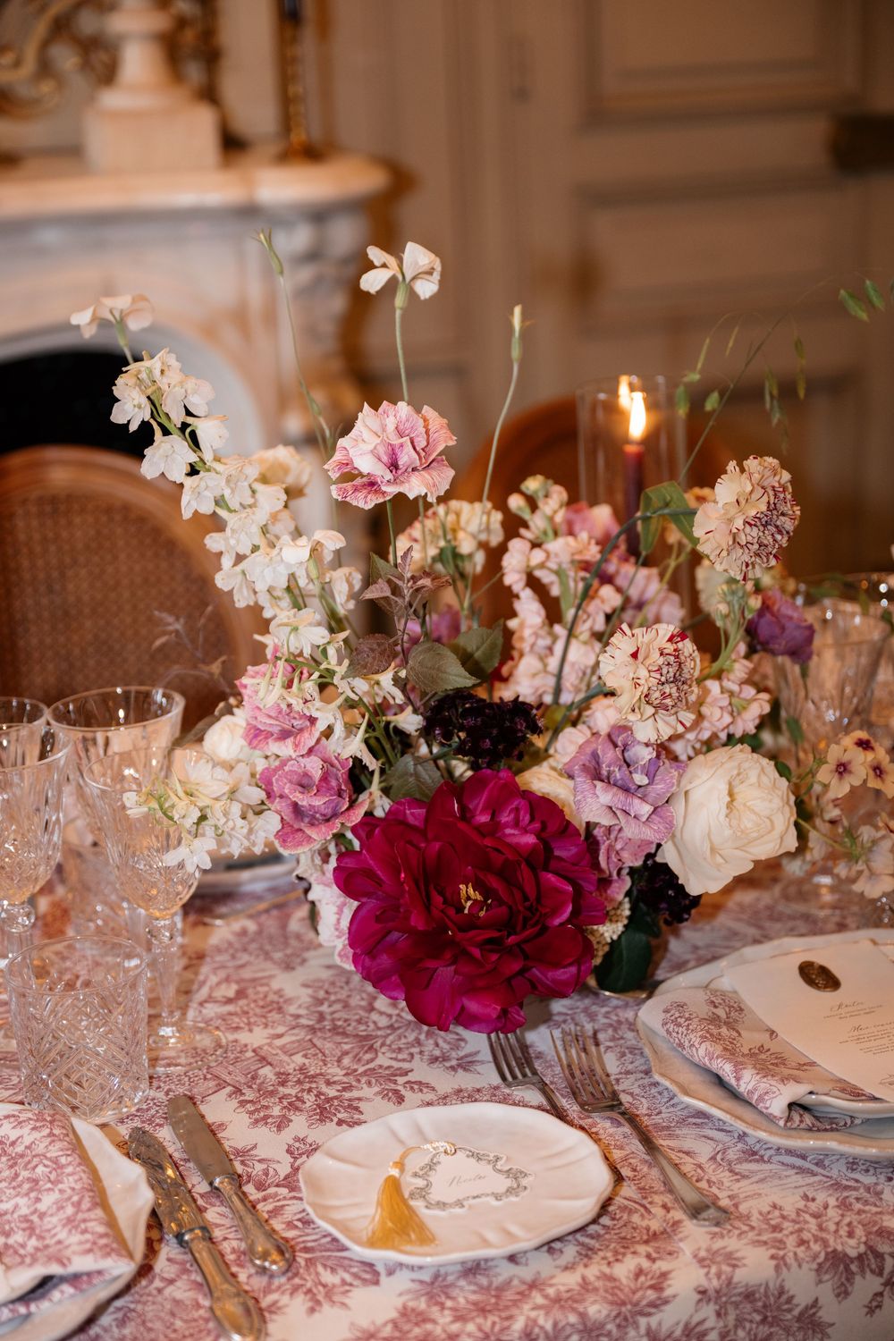 Elegant table setting with pink floral arrangements, crystal glassware, and delicate place settings on patterned tablecloth.