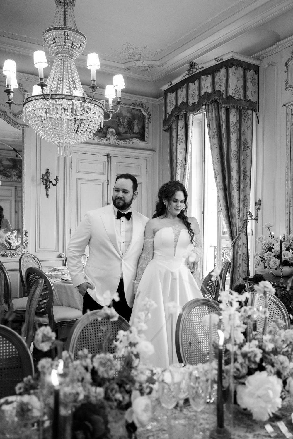 Elegant wedding reception setup in a grand room with crystal chandeliers, ornate decor, and floral arrangements.