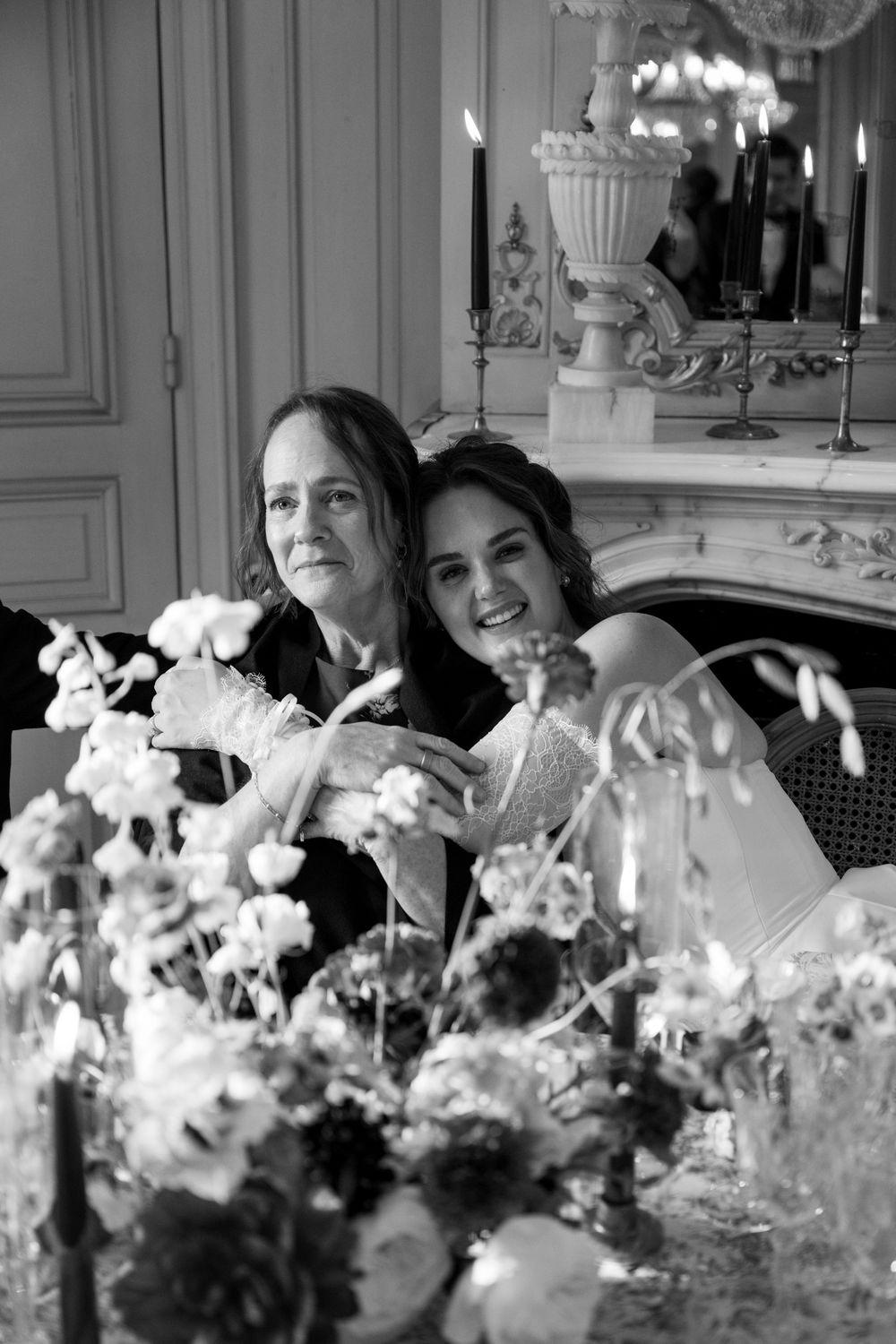 Black and white photo of people sitting at an elegant dining table with floral centerpieces and crystal chandeliers.