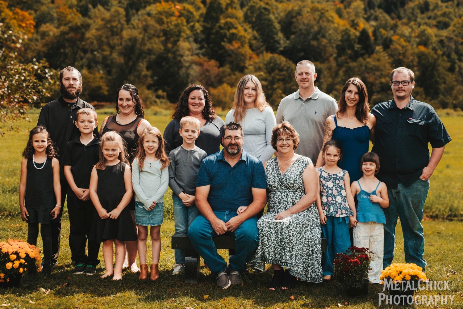 Family portrait by Northern Exposure featuring a large family sitting in front of a mountainous tree filled background.
