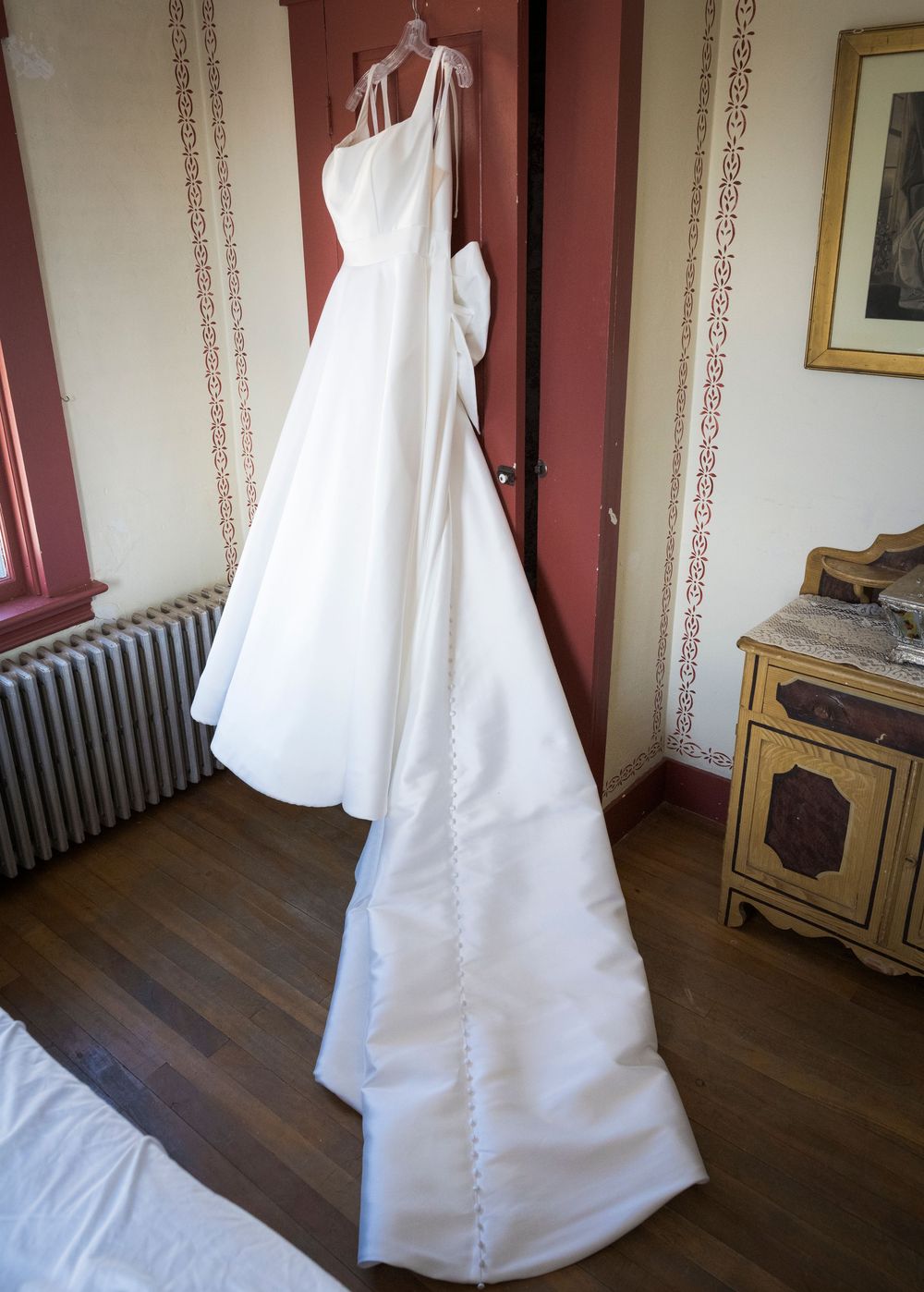 White wedding dress hanging in a vintage room with dark wood floors and burgundy walls.