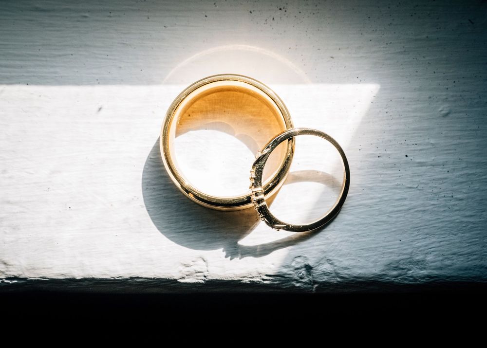 Gold wedding rings casting dramatic shadows on a white surface in a creative photo series.