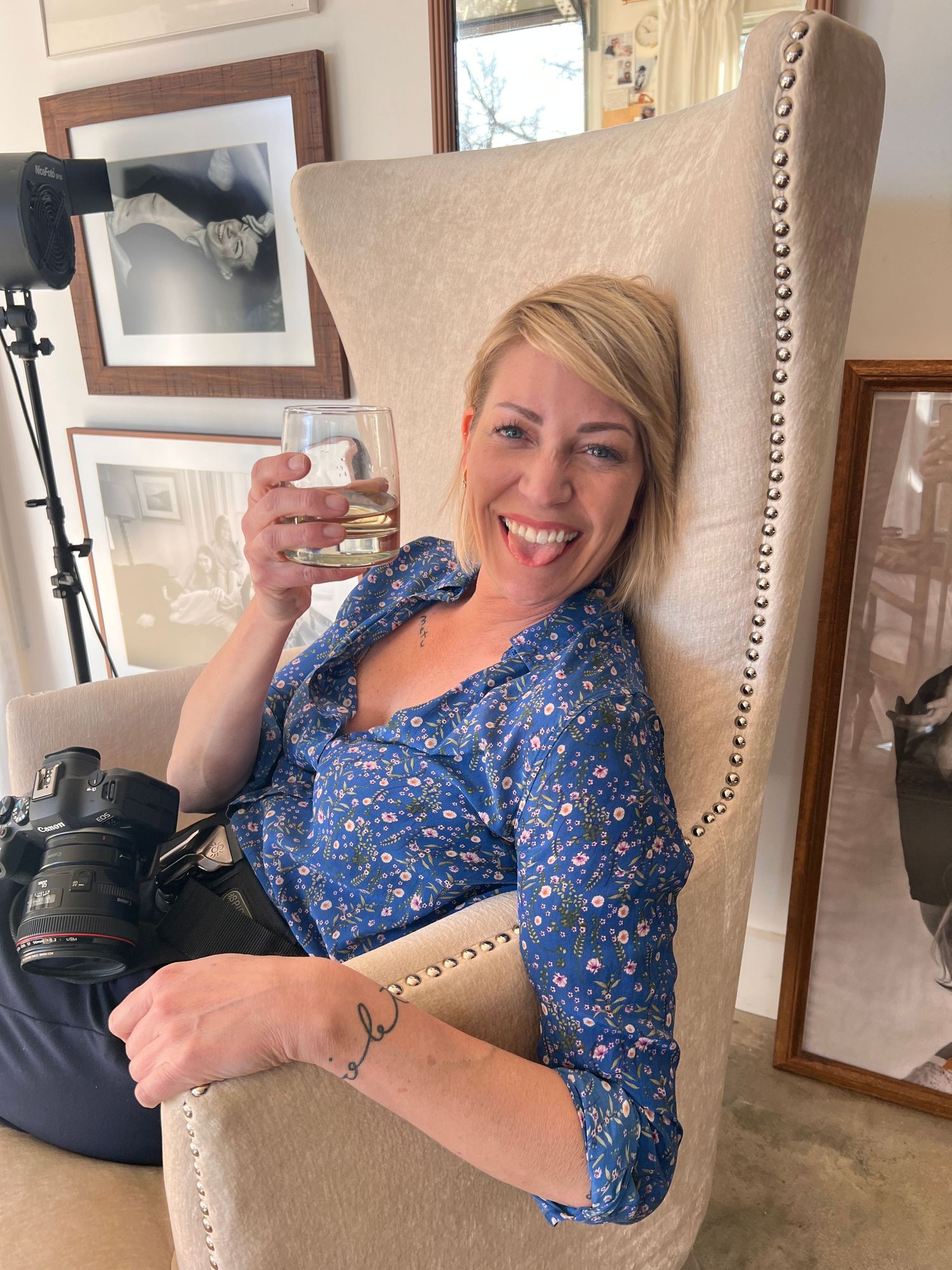 A person in a blue floral dress sits casually on a beige upholstered chair in a home setting.