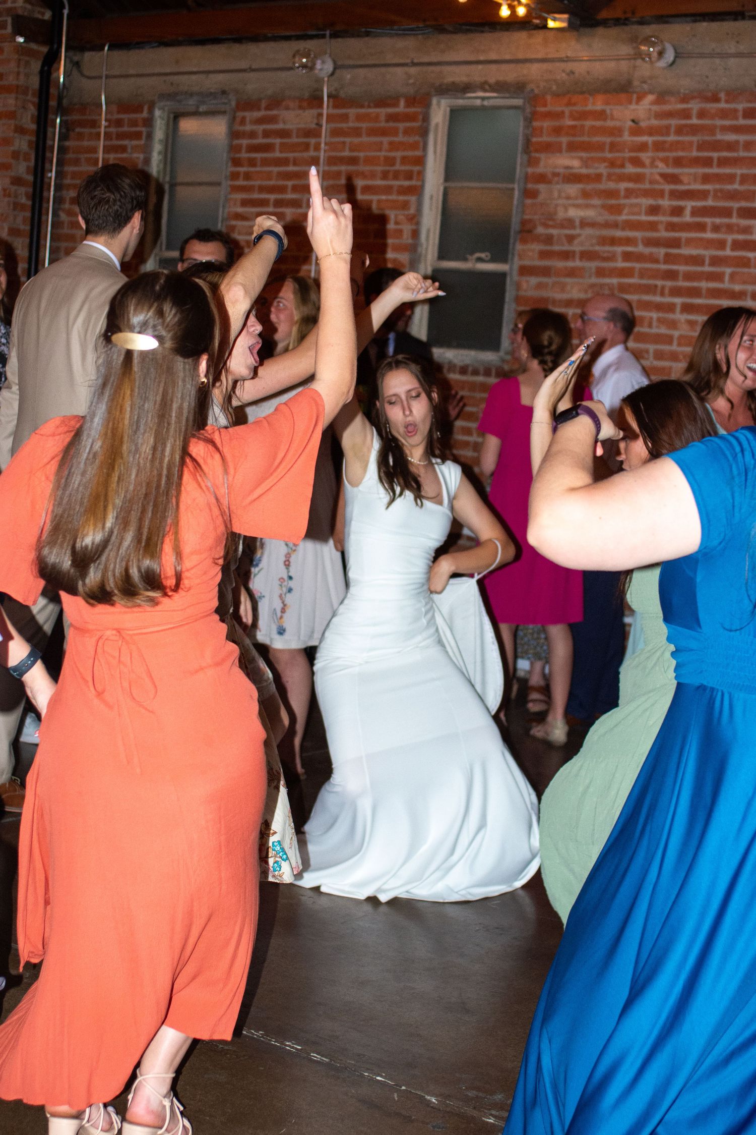Wedding reception guests dance together in rustic brick venue with string lights in Salt Lake City, Utah.