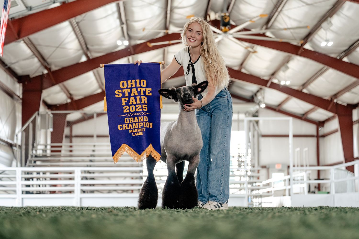 A person holding a blue championship banner poses with a black horse in a covered equestrian arena.