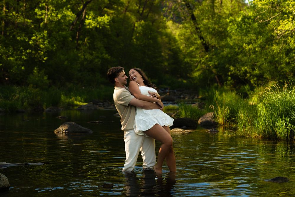 Romantic couple sits at edge of tranquil pond surrounded by lush greenery.