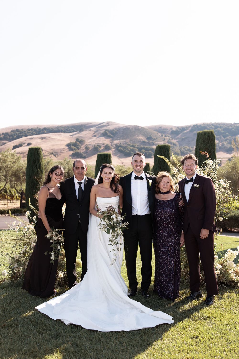 Wedding party poses together outdoors with scenic mountain backdrop during sunset celebration.