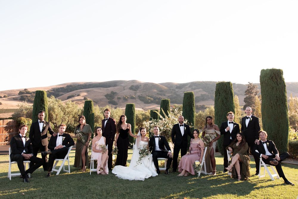 Wedding party poses together on a scenic hillside with cypress trees and rolling hills in the background.