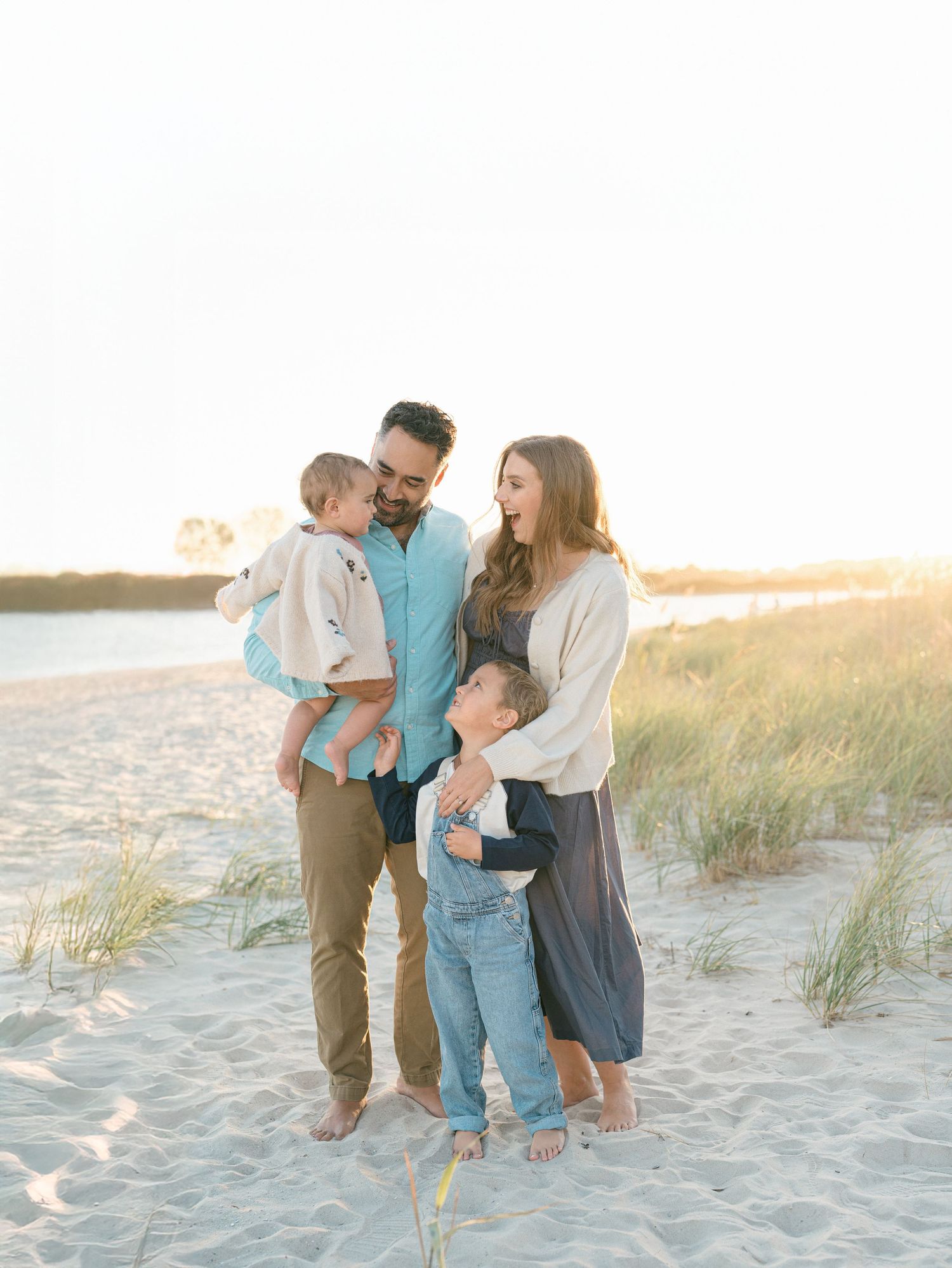 A family snuggles close and looks at one another while lauren marie photography documents them on a nj beach.