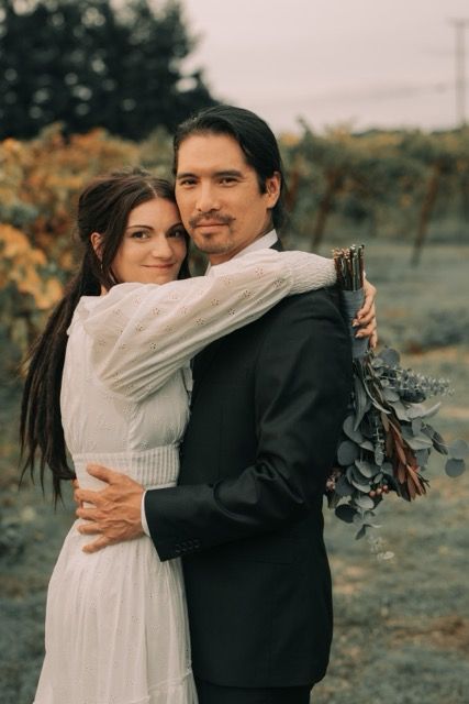 A romantic couple embraces outdoors in wedding attire during a fall photoshoot with muted earth tones.