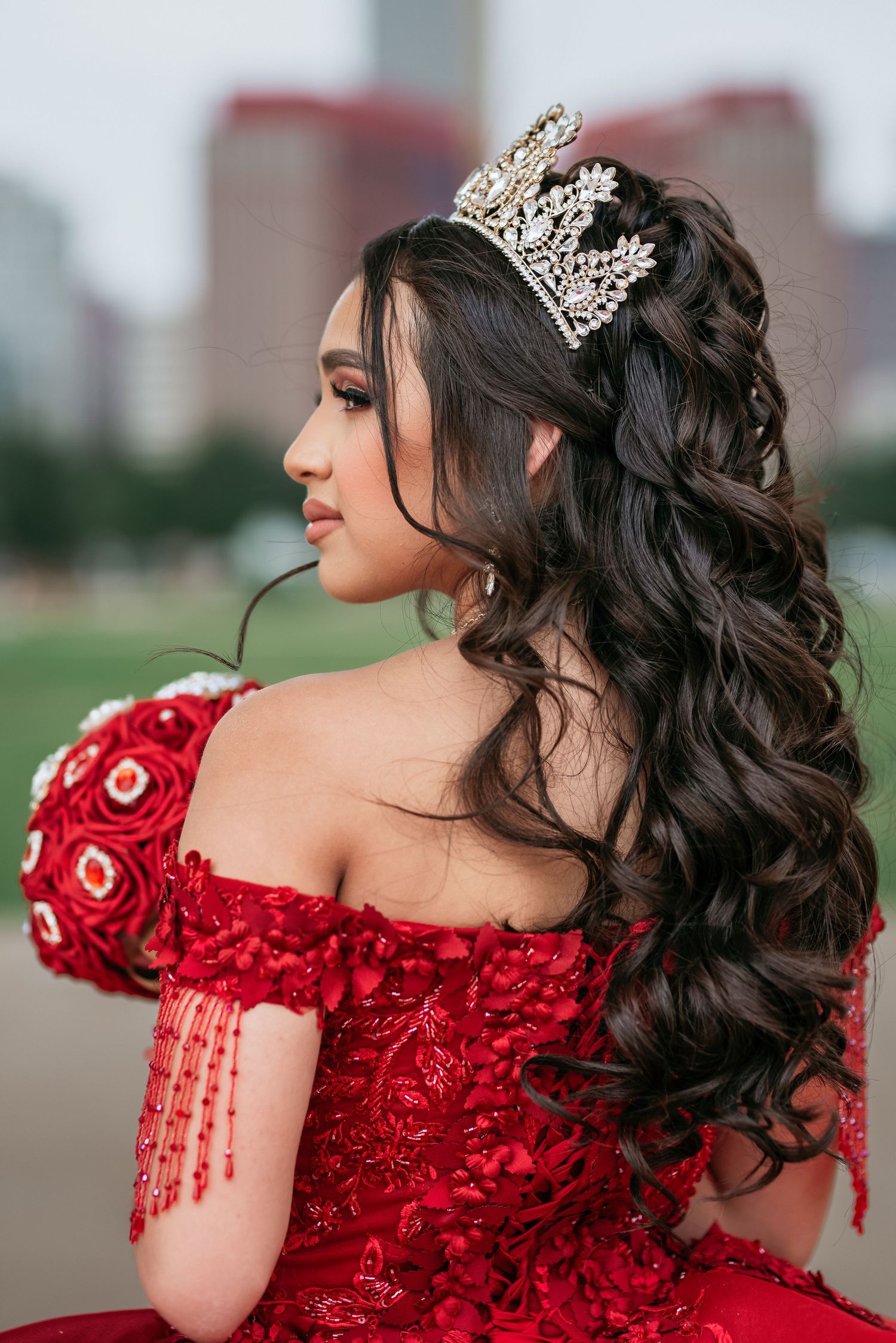 A detailed view of an ornate crown and styled dark curls against a formal red dress.