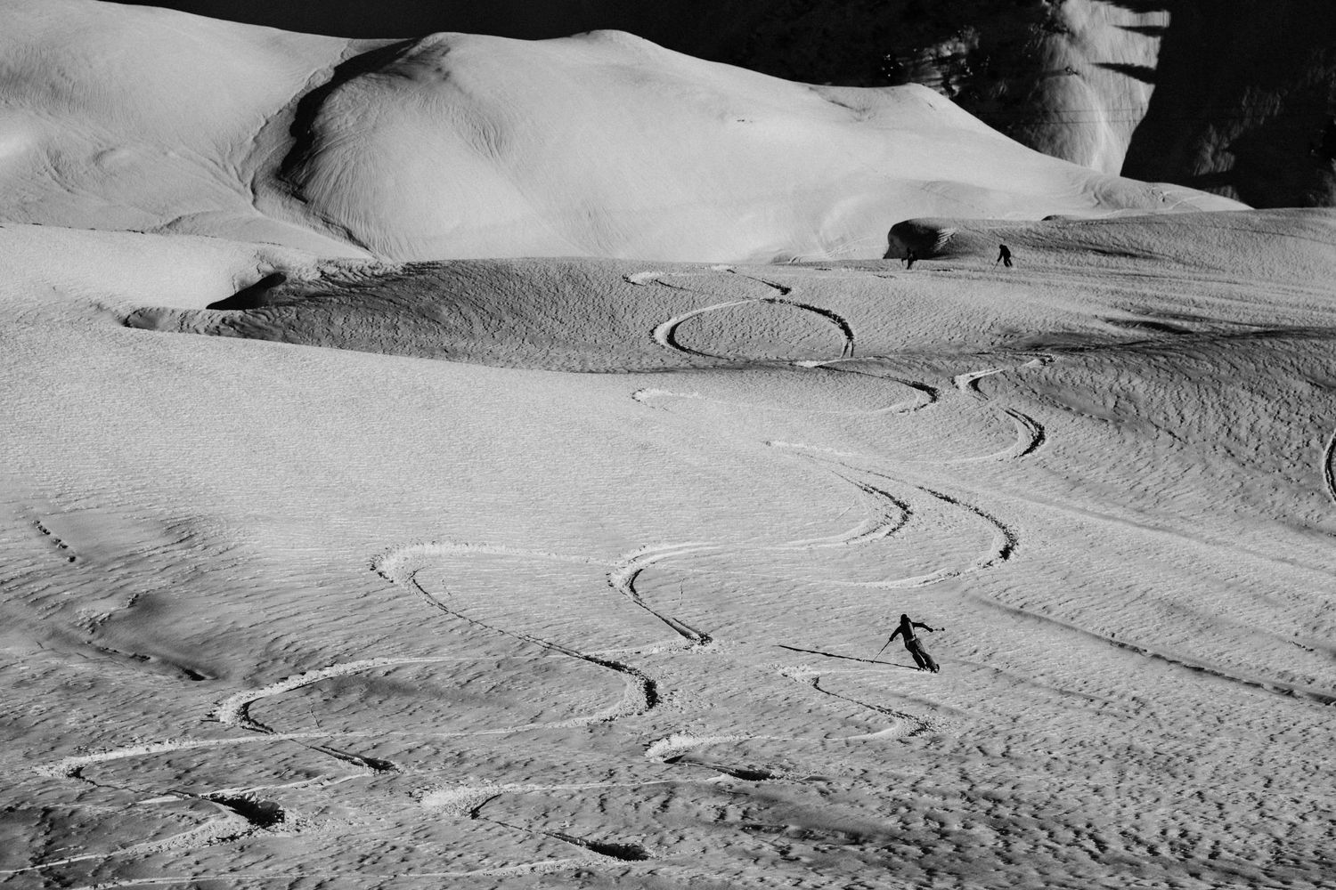 A sequence of black and white aerial photographs showing ski tracks winding through fresh powder snow on mountain slopes.