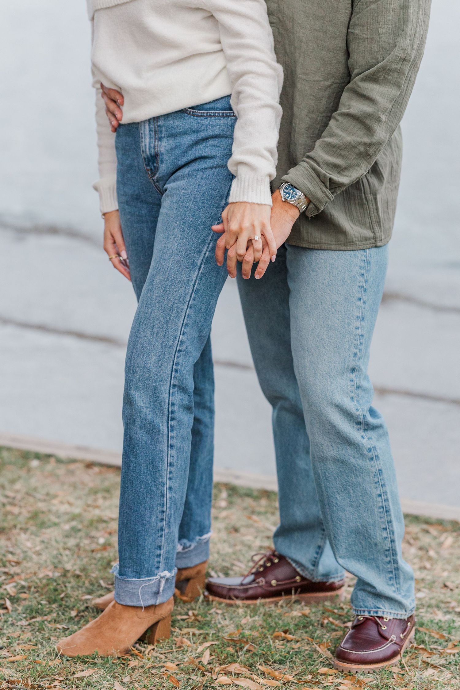 Close-up view of two people's legs wearing jeans and contrasting shoes, one in brown boots and one in burgundy oxfords.