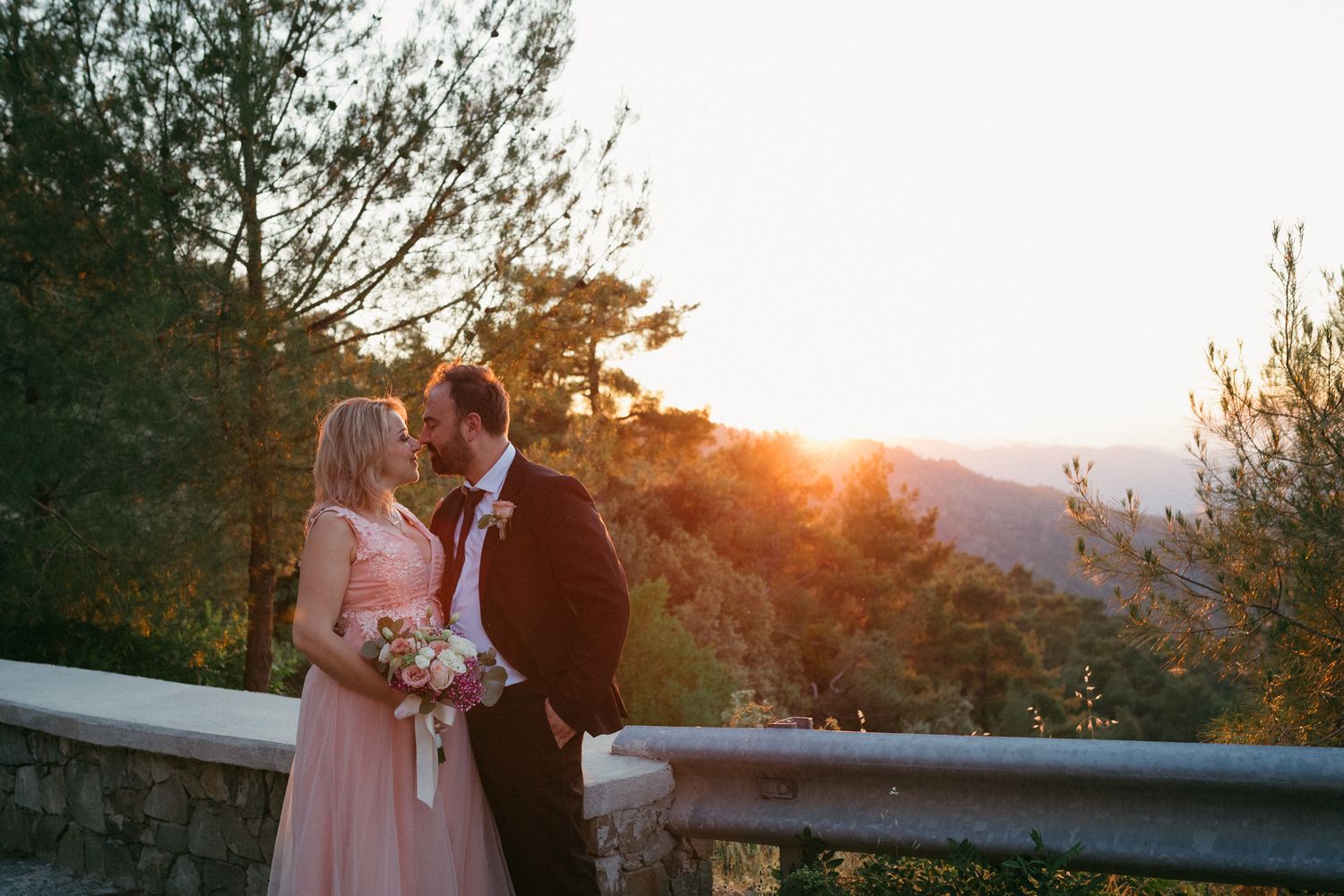 A romantic sunset wedding photo session with pink and orange hues illuminating a mountainous backdrop.