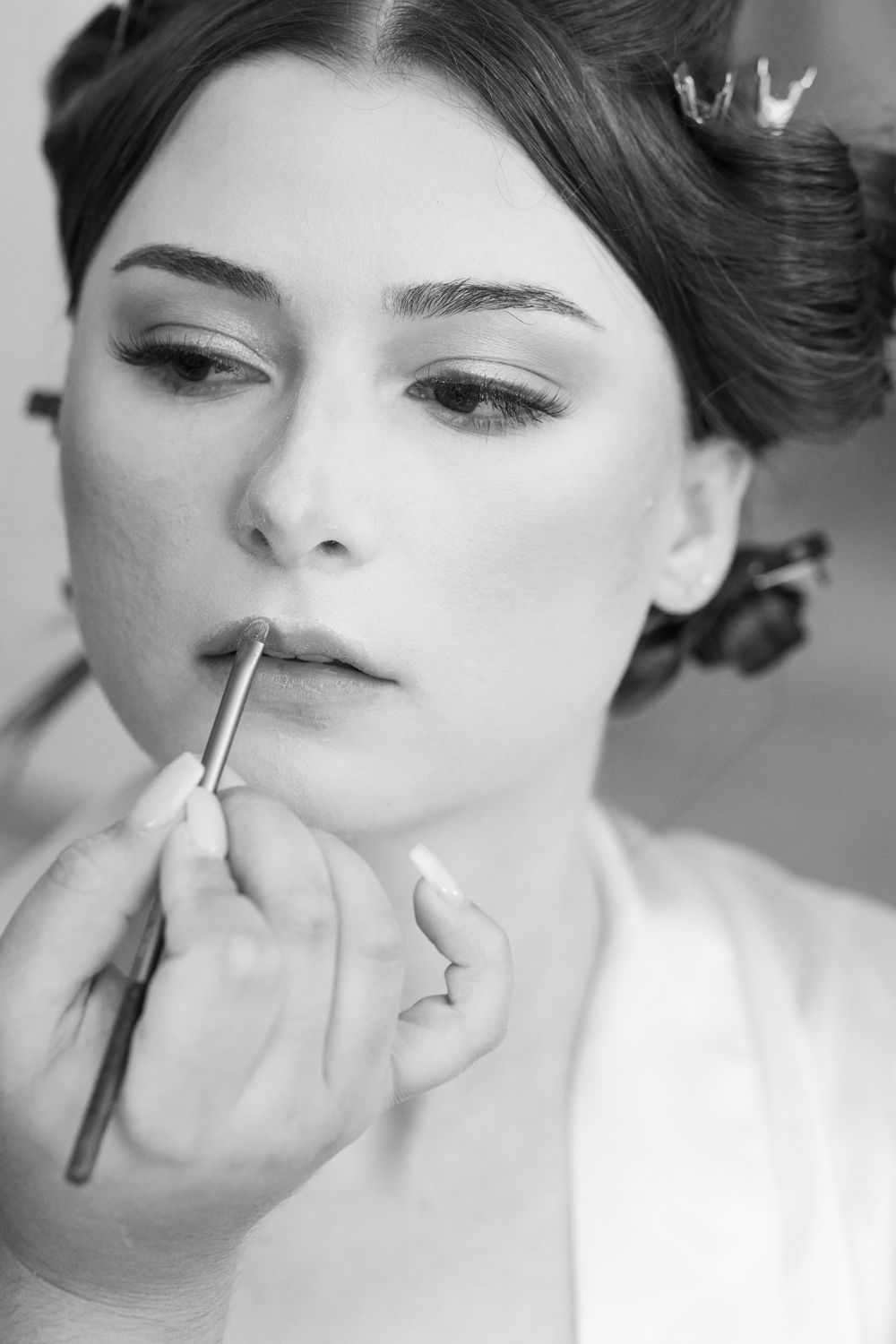 A black and white photo series showing the application of makeup and cosmetics in a professional beauty setting.