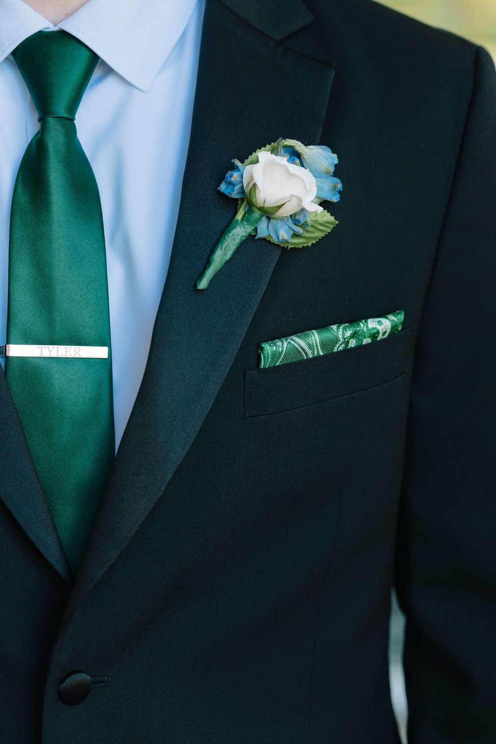 Groomsmen wearing black suits with emerald green ties and white rose boutonnieres lined up at a formal wedding.
