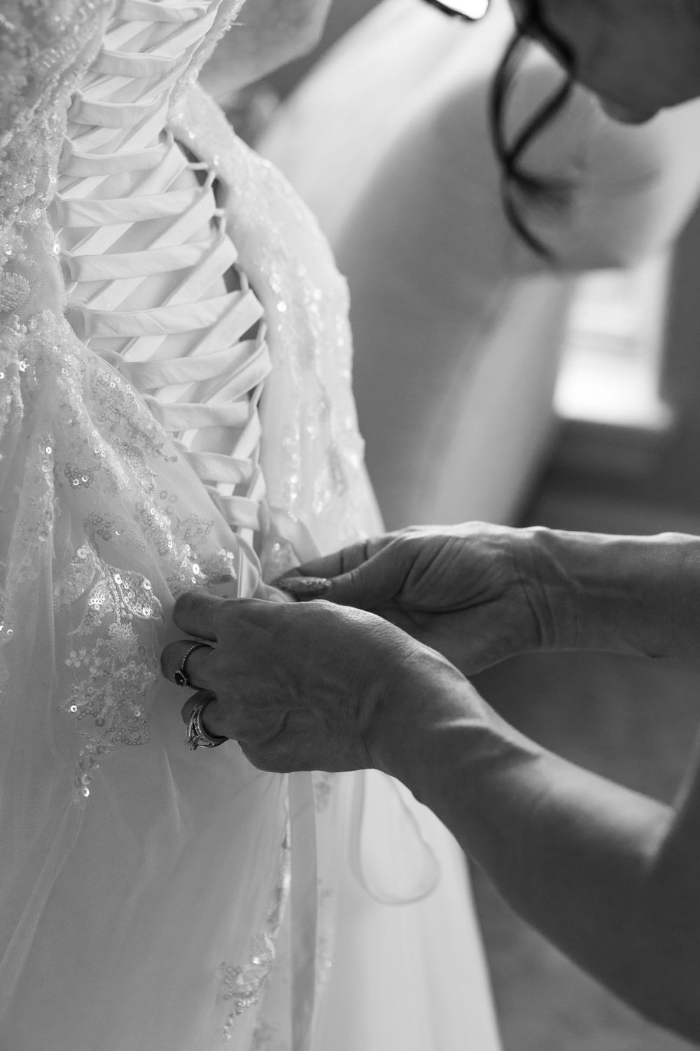Close-up black and white photo of hands adjusting details on a white lace wedding dress.