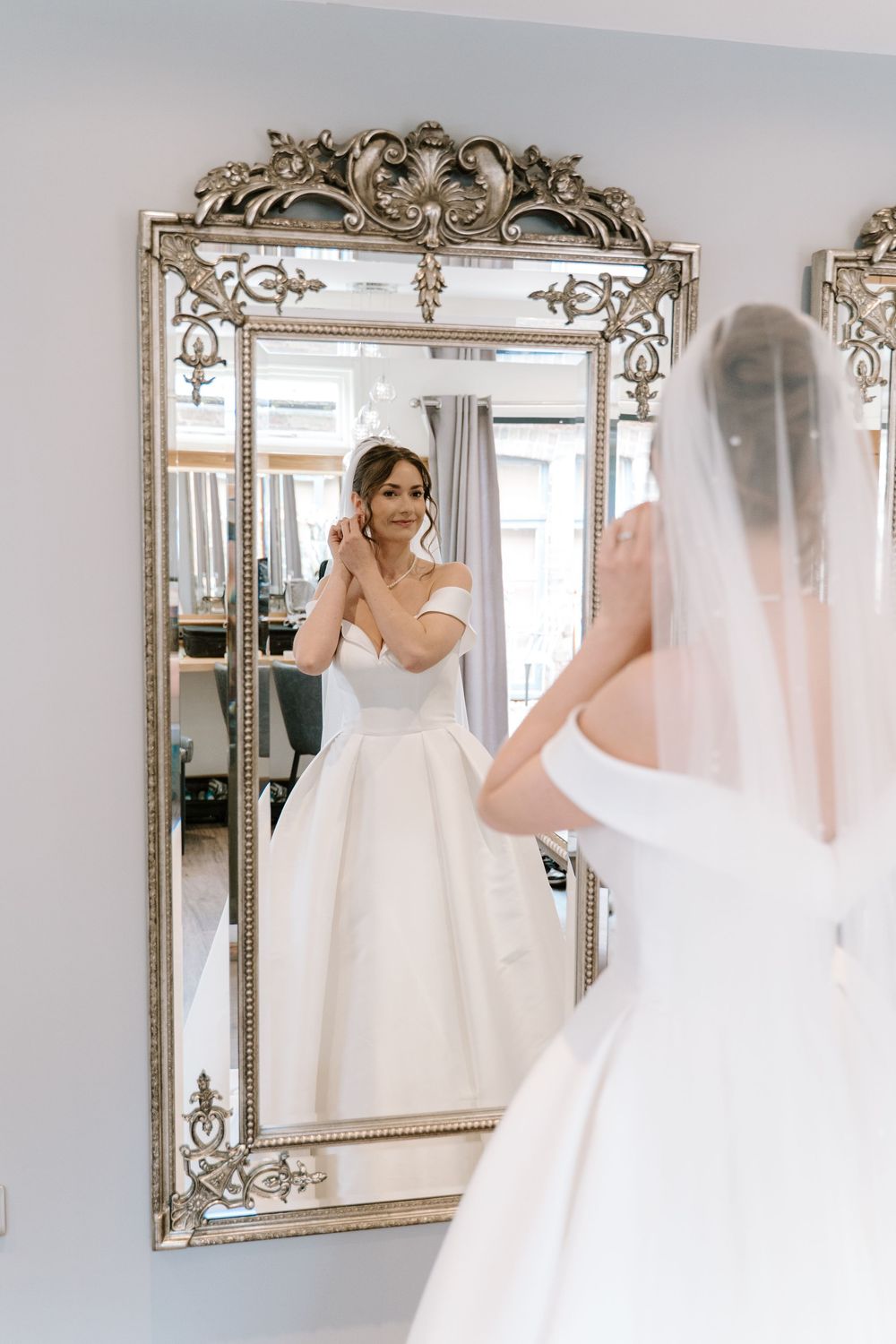 Elegant ornate mirrors reflect a Worcestershire bride in a white wedding gown during a bridal fitting session.