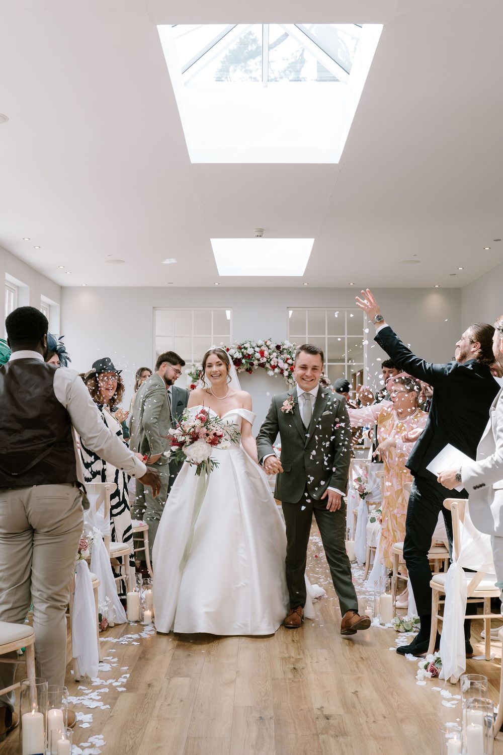 Bredenbury Court Barns Wedding guests celebrate by throwing confetti at a newlywed couple in a bright indoor venue with wooden floors.