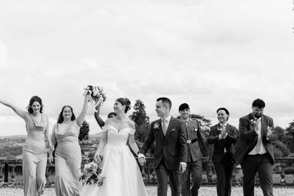 Black and white wedding party celebrating outdoors with joyful expressions and raised arms.