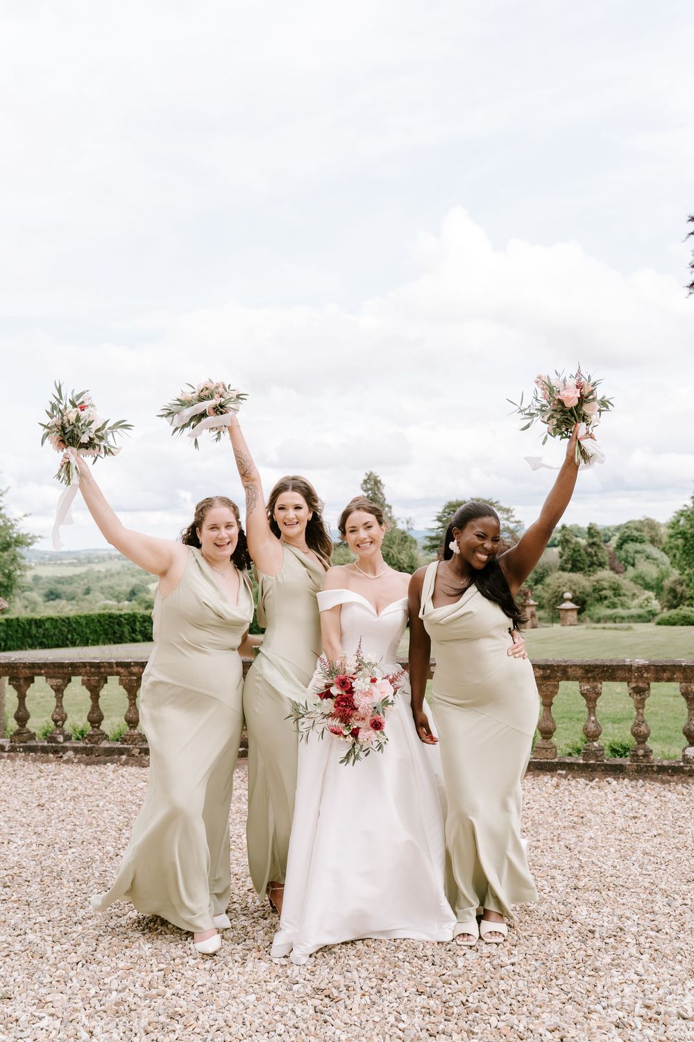 Worcestershire Bridal party in cream-colored dresses celebrates joyfully on a gravel terrace with garden views.