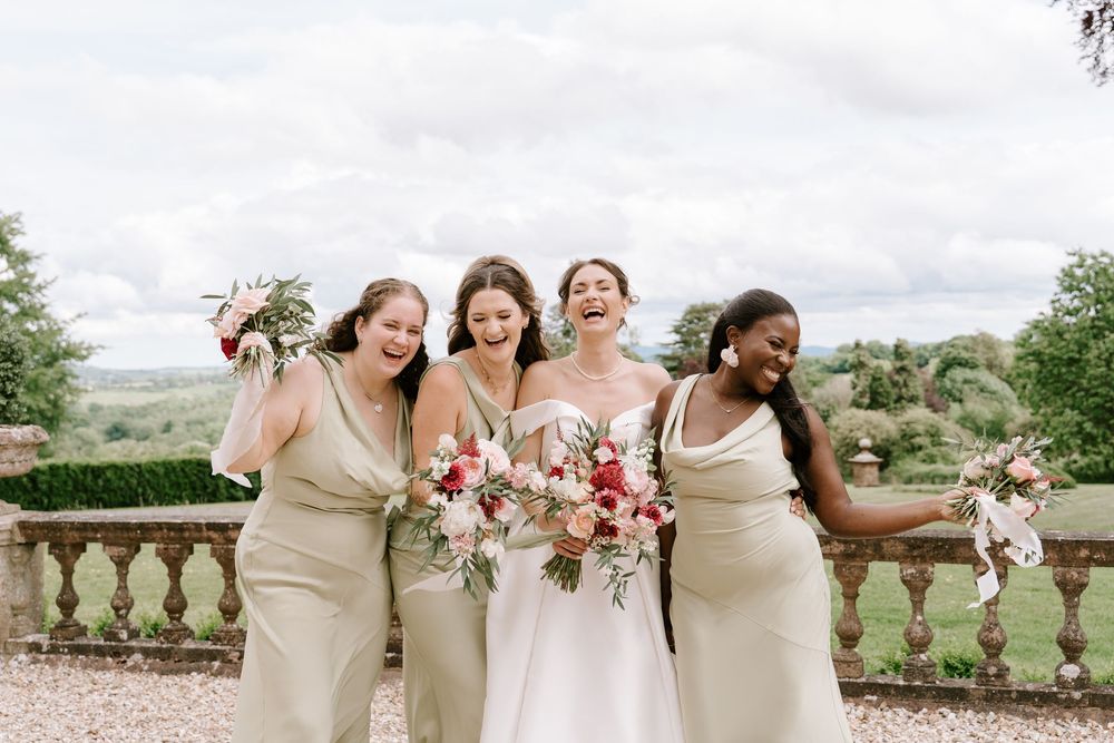 Bridesmaids in cream dresses pose together with pink bouquets at an elegant outdoor wedding venue.