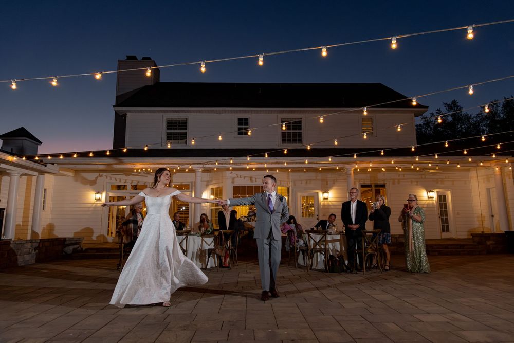 String lights illuminate an outdoor evening wedding reception venue with tables and chairs set up on a patio.
