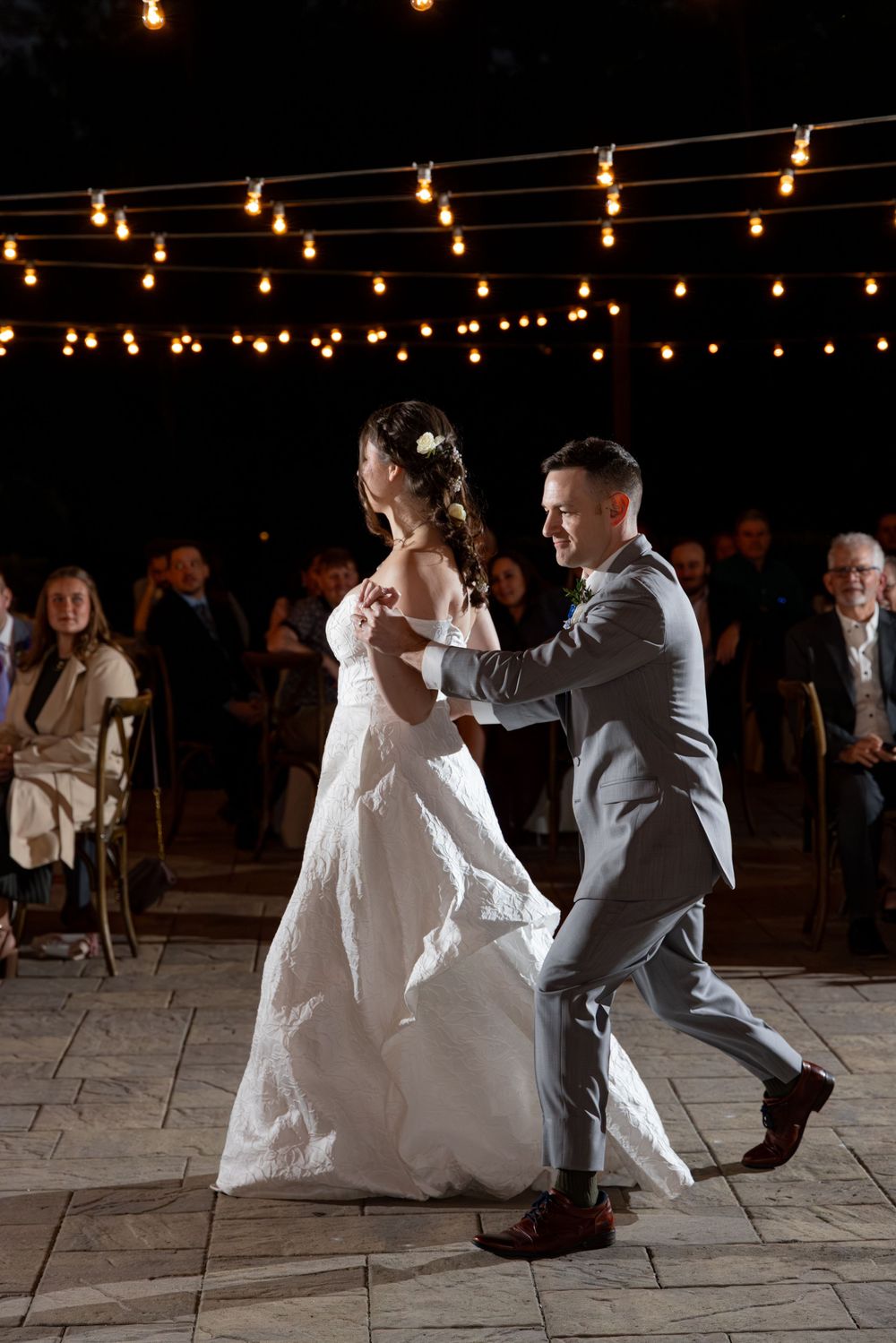 Couple performs a dramatic dip dance move under twinkling string lights at their wedding reception.