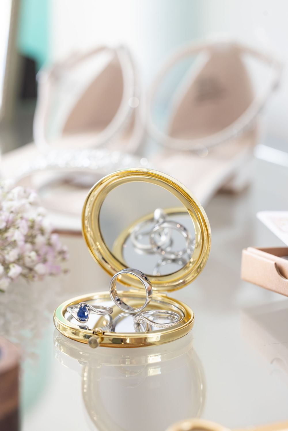 Elegant gold-rimmed jewelry box with delicate floral details and blue gemstone accent on a light surface.