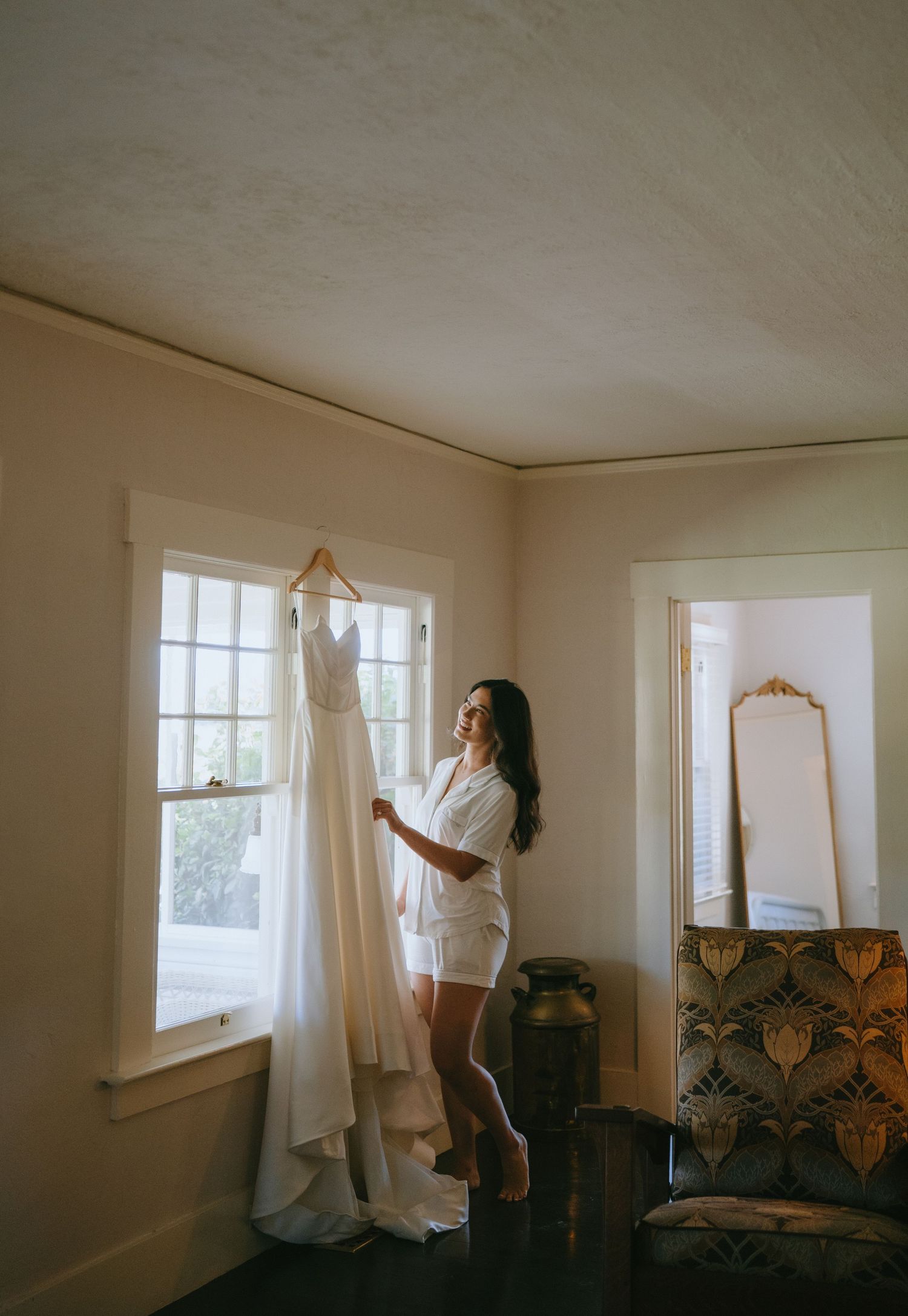 Black and white photo of bride in lace gown with cathedral veil gazing out a window.