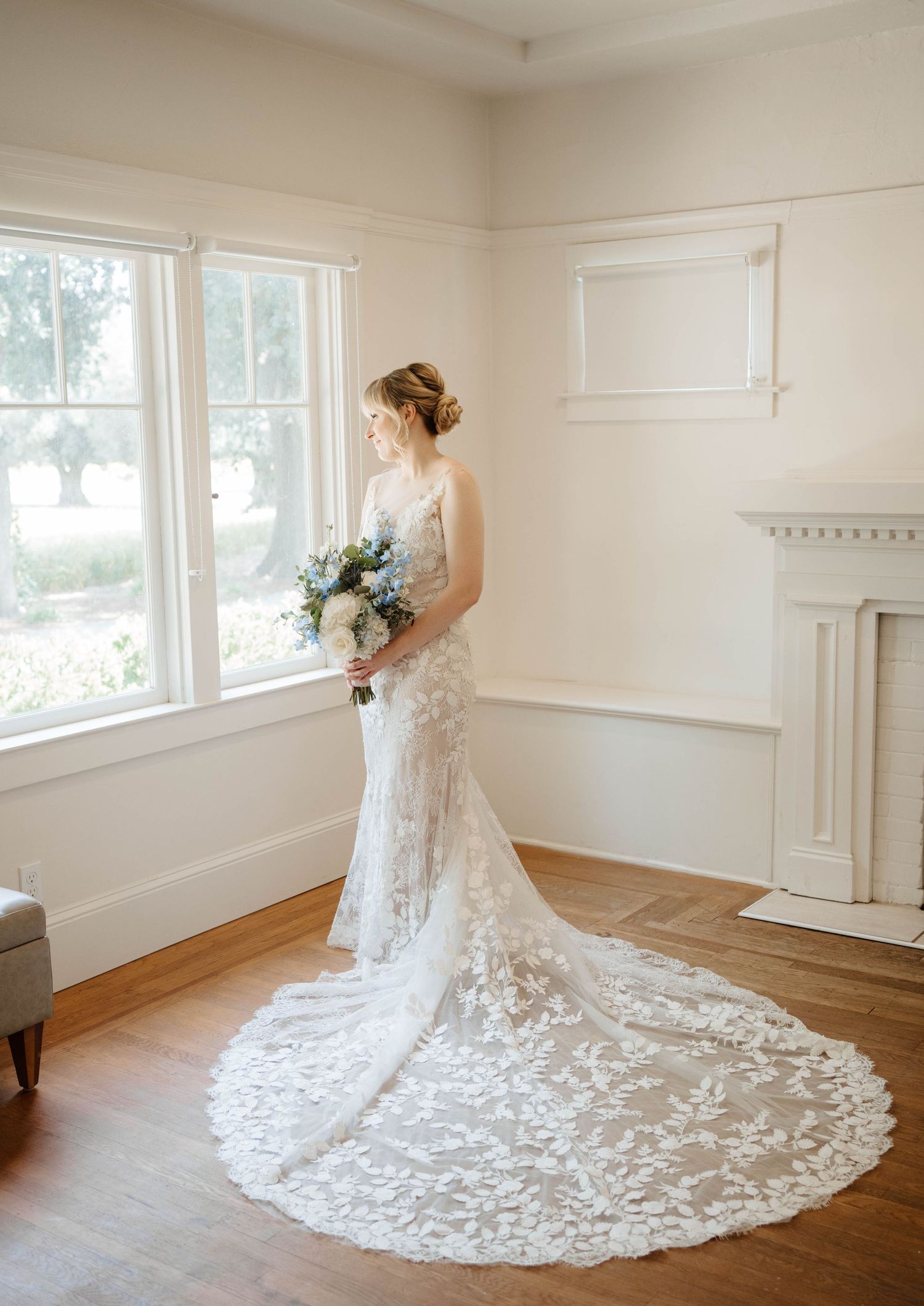 Black and white photo of bride in lace gown with cathedral veil gazing out a window.