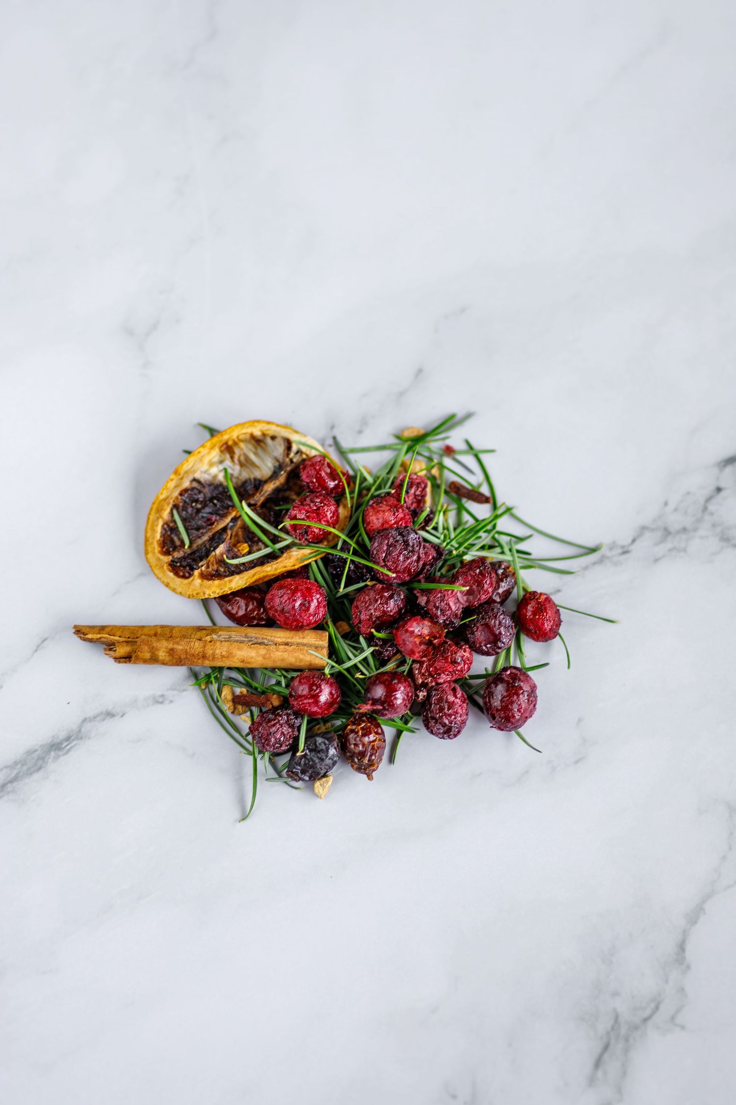 Fresh red raspberries with dried orange slices and rosemary garnish on white marble surface.