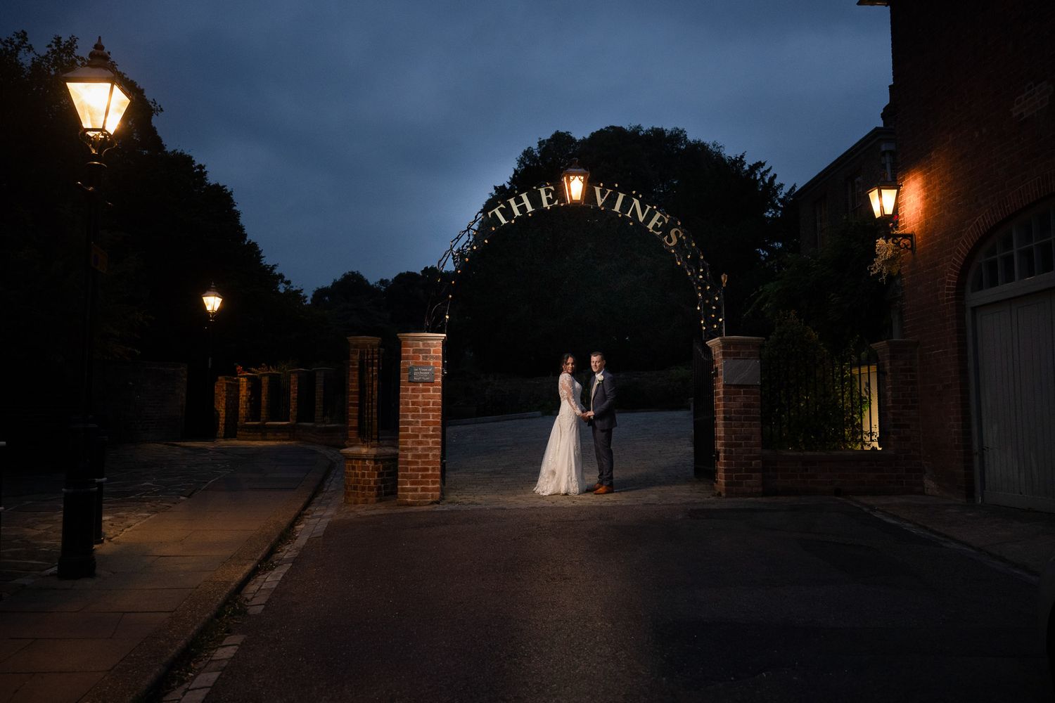 A bride and groom portrait under a glowing lamp post at dusk in a romantic outdoor setting at The Vines wedding venue in Rochester.