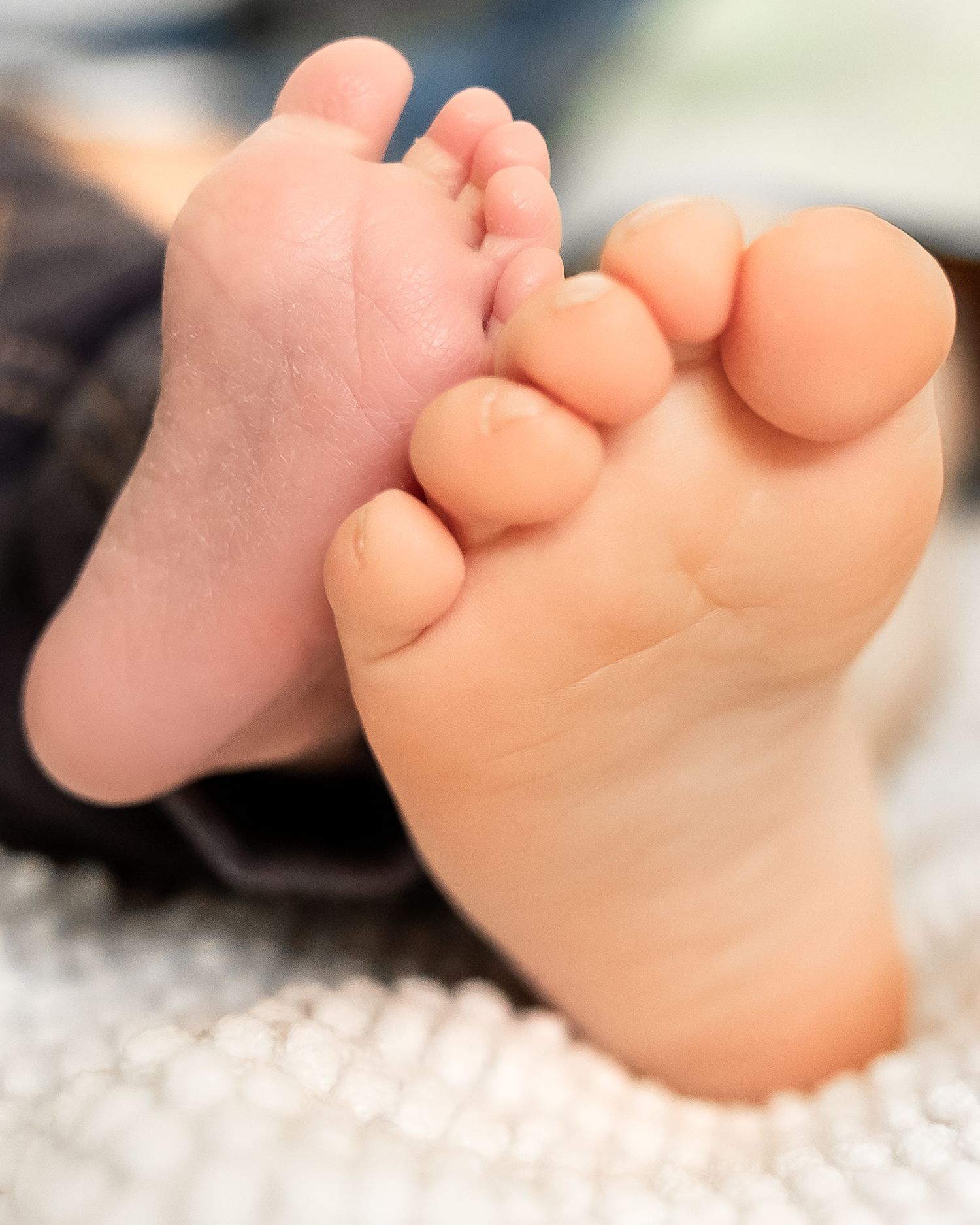 Close-up macro shots of tiny baby feet on white textured fabric showing delicate toes and soft skin.