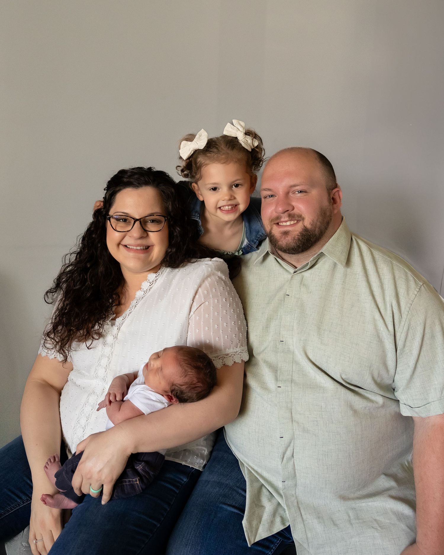 A family portrait showing parents with their two children against a neutral gray background.