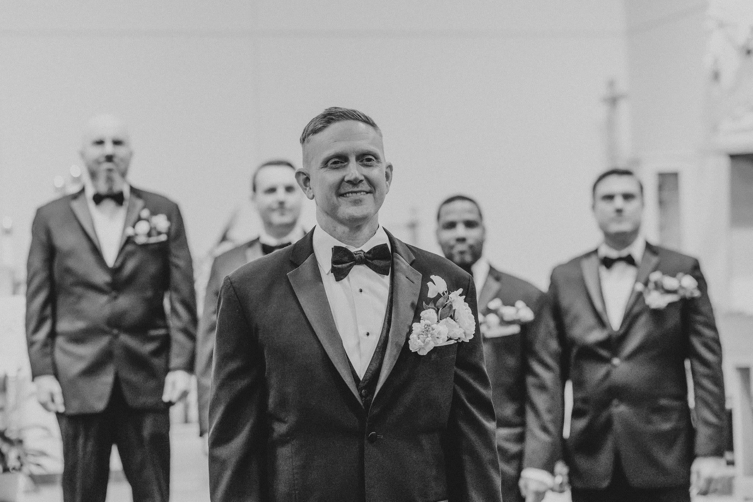 Black and white photo of groomsmen in suits posing together outdoors with joyful expressions.