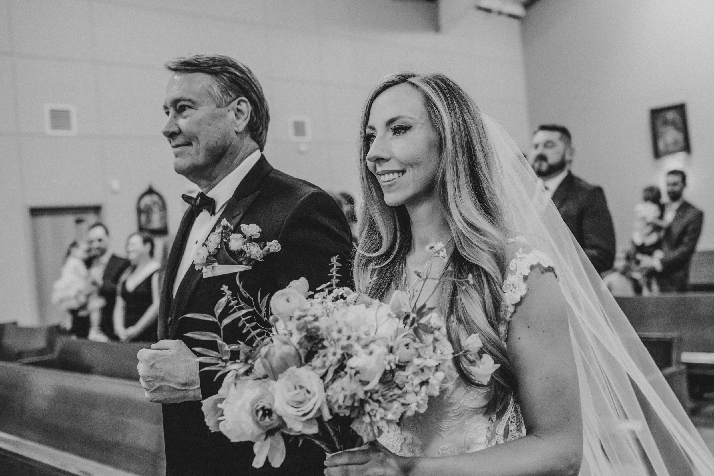 A joyful moment captured in black and white as a bride walks down the church aisle with her bouquet of flowers.