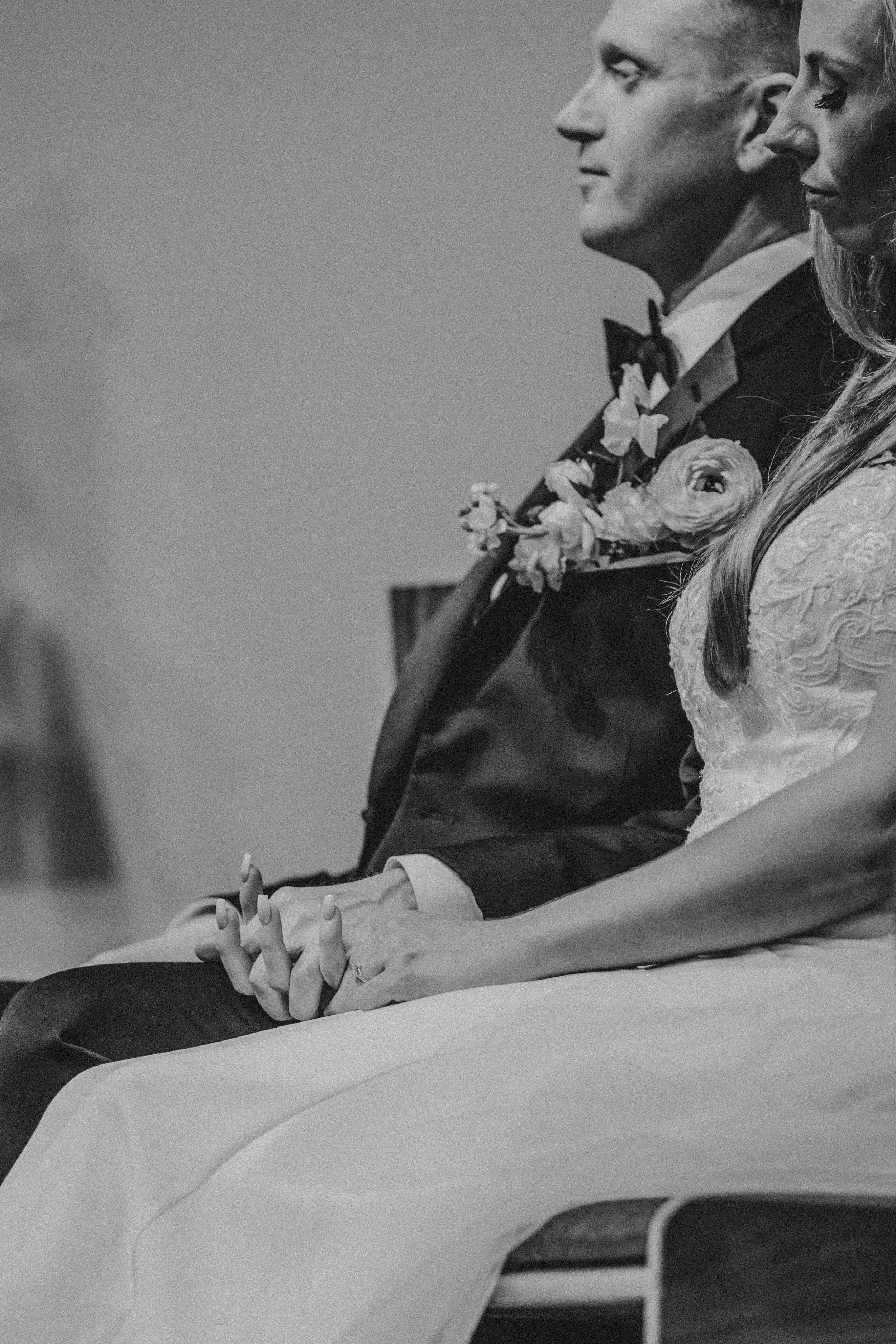 Black and white wedding photo showing couple seated together in formal attire during ceremony.