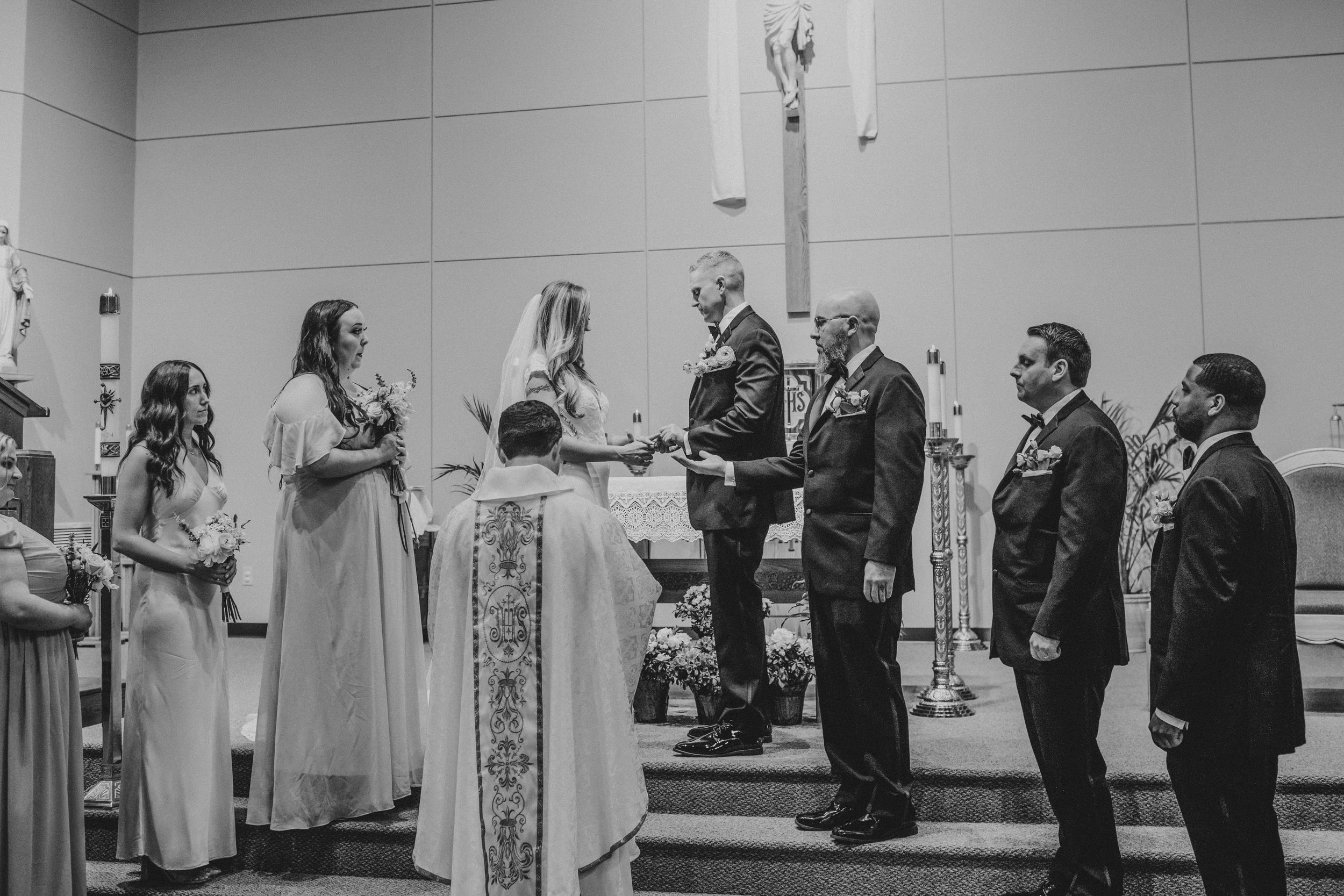 A black and white wedding ceremony photo showing a group gathered at the altar in a church setting.