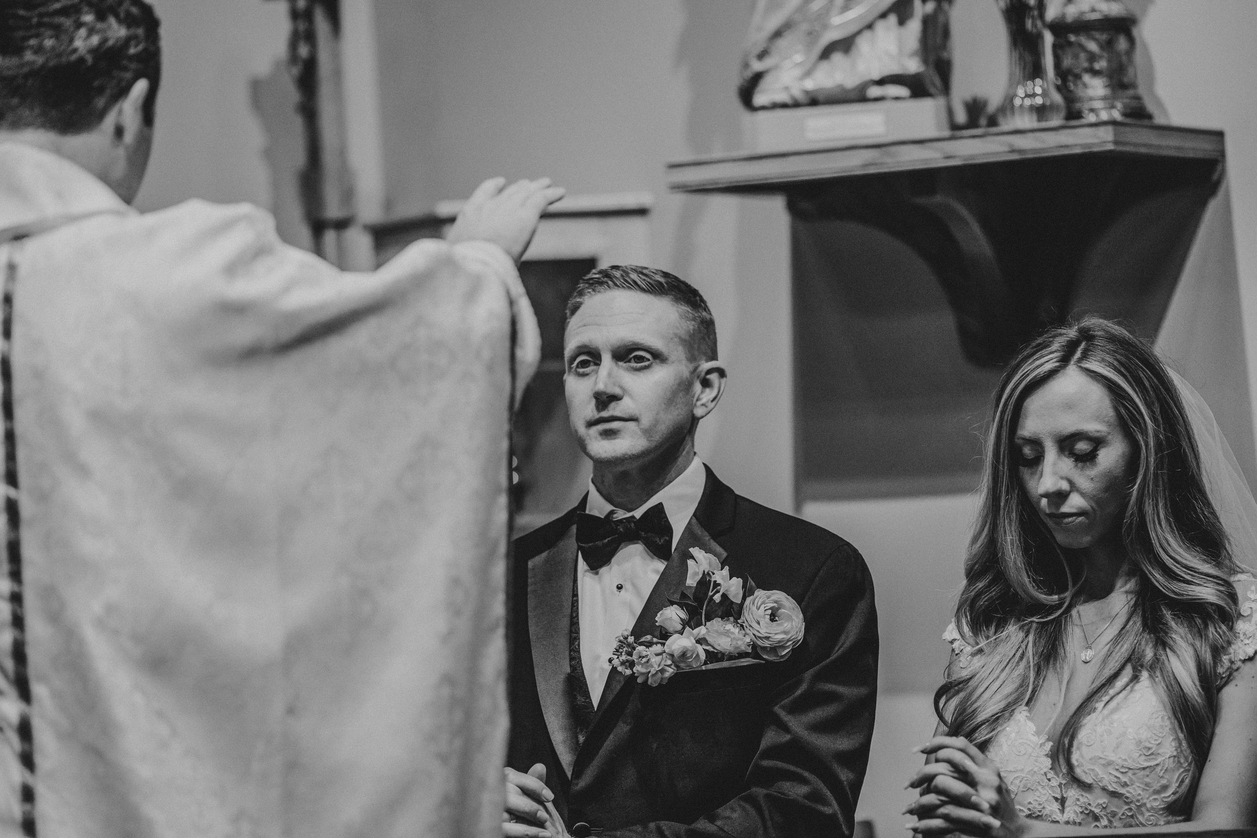 A black and white photograph capturing a solemn wedding ceremony with a priest officiating.