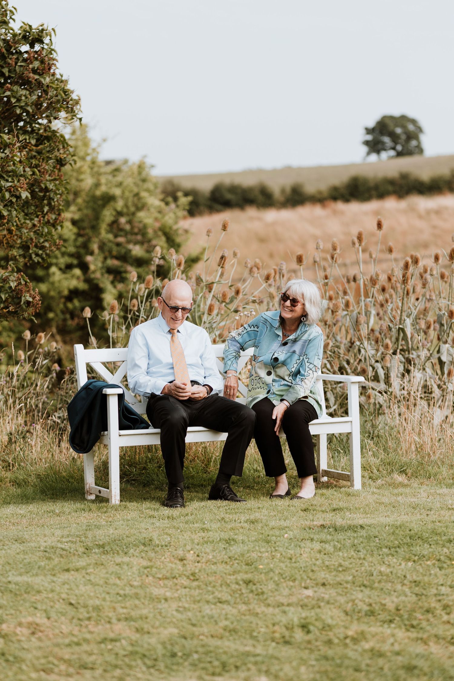 Two people sit together on a white wooden bench during drinks reception at Lyde Court, Hereford.